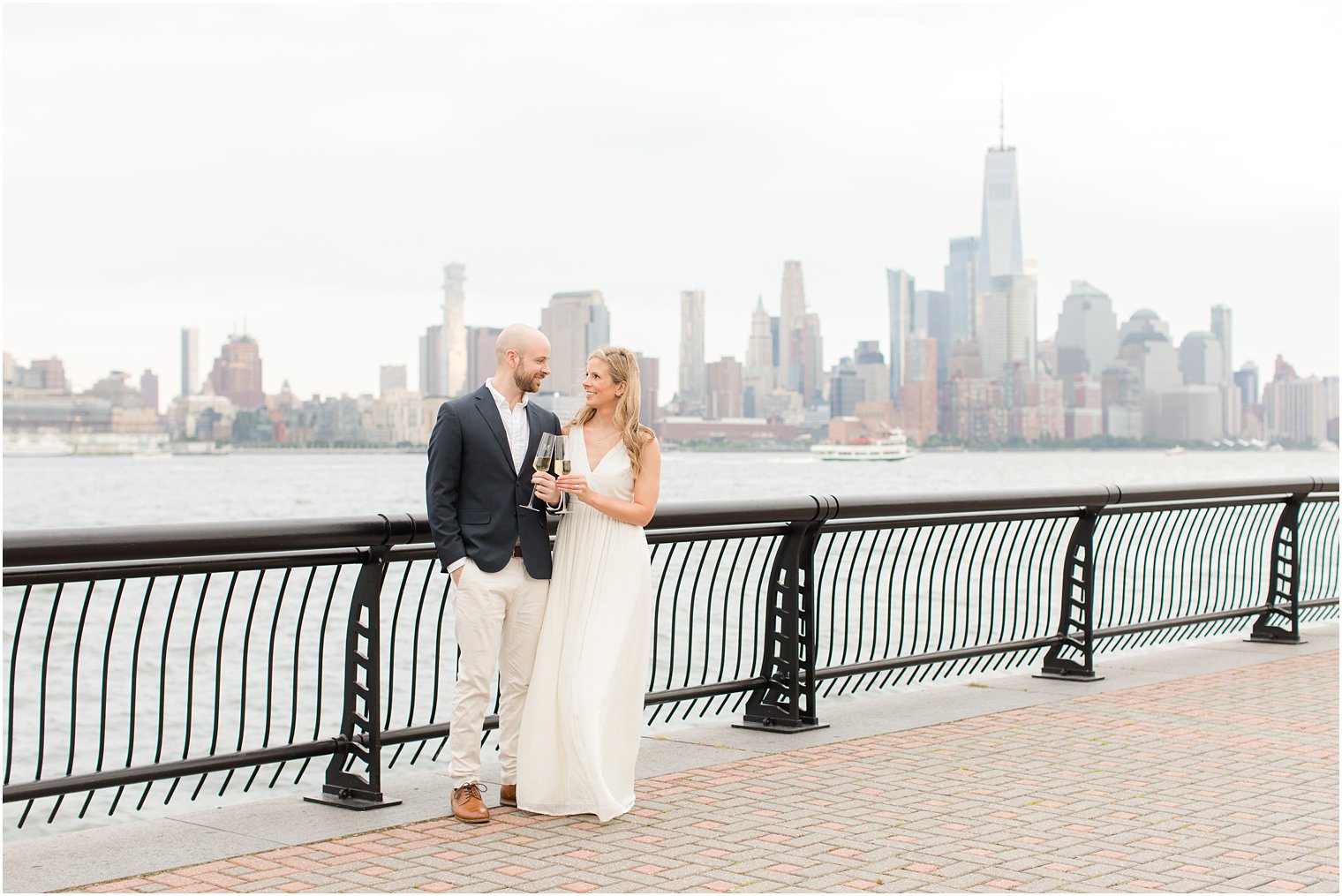 engaged couple toasts champagne along waterfront in New Jersey