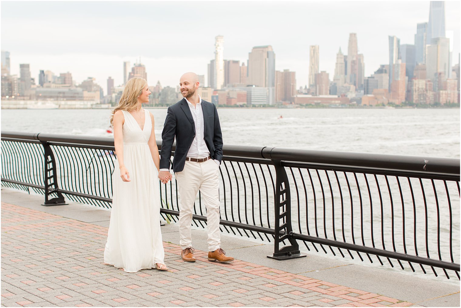 engaged couple holds hands walking along waterfront in New Jersey