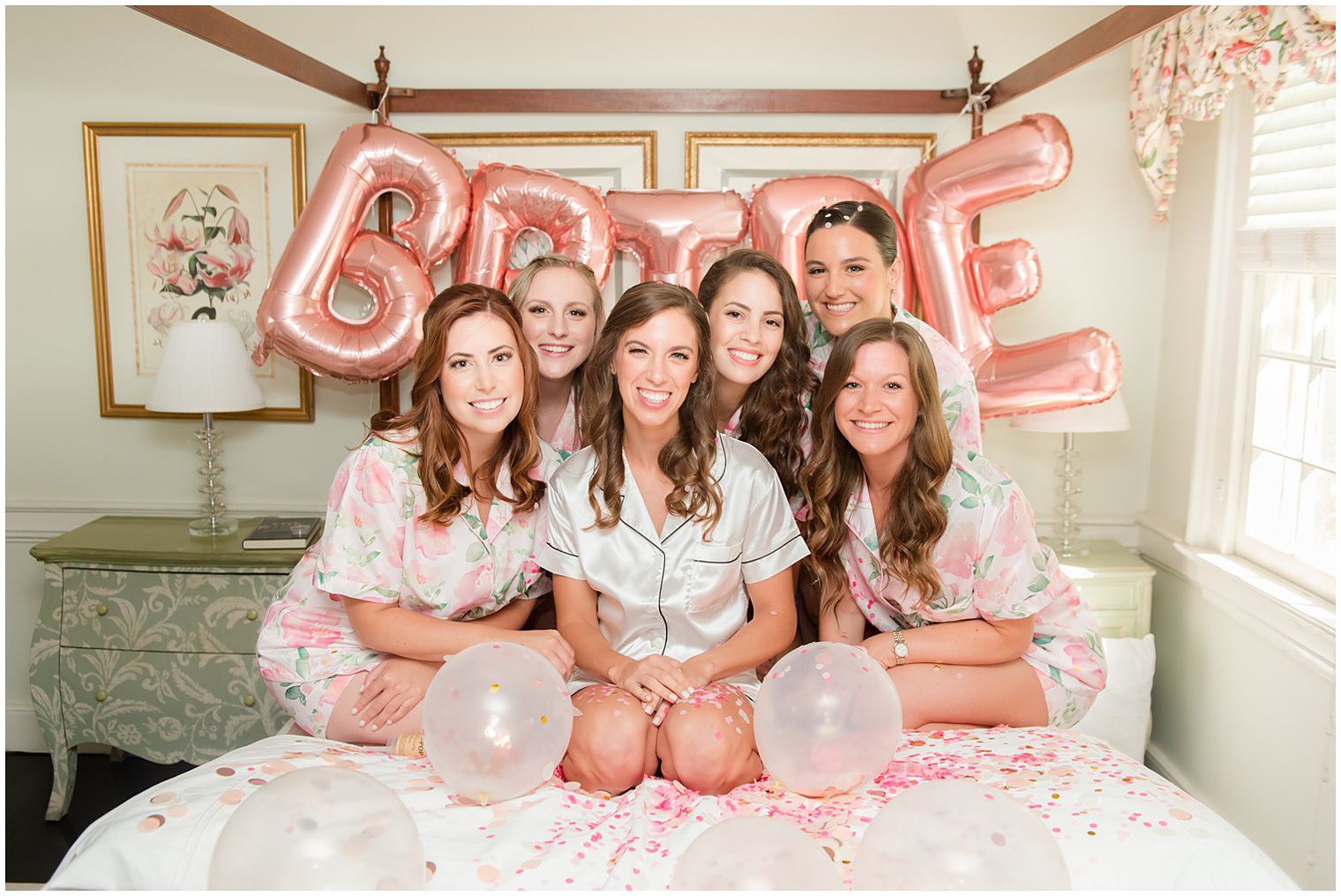 bride and bridesmaids sit on bed together during wedding prep