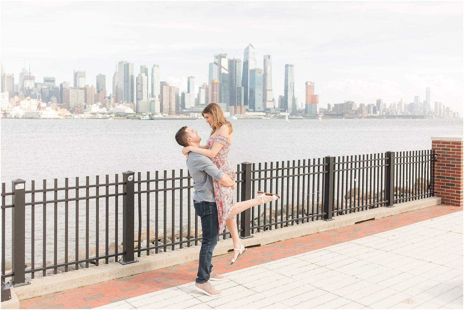 groom lifts bride during Weehawken waterfront engagement session with NYC skyline behind them 