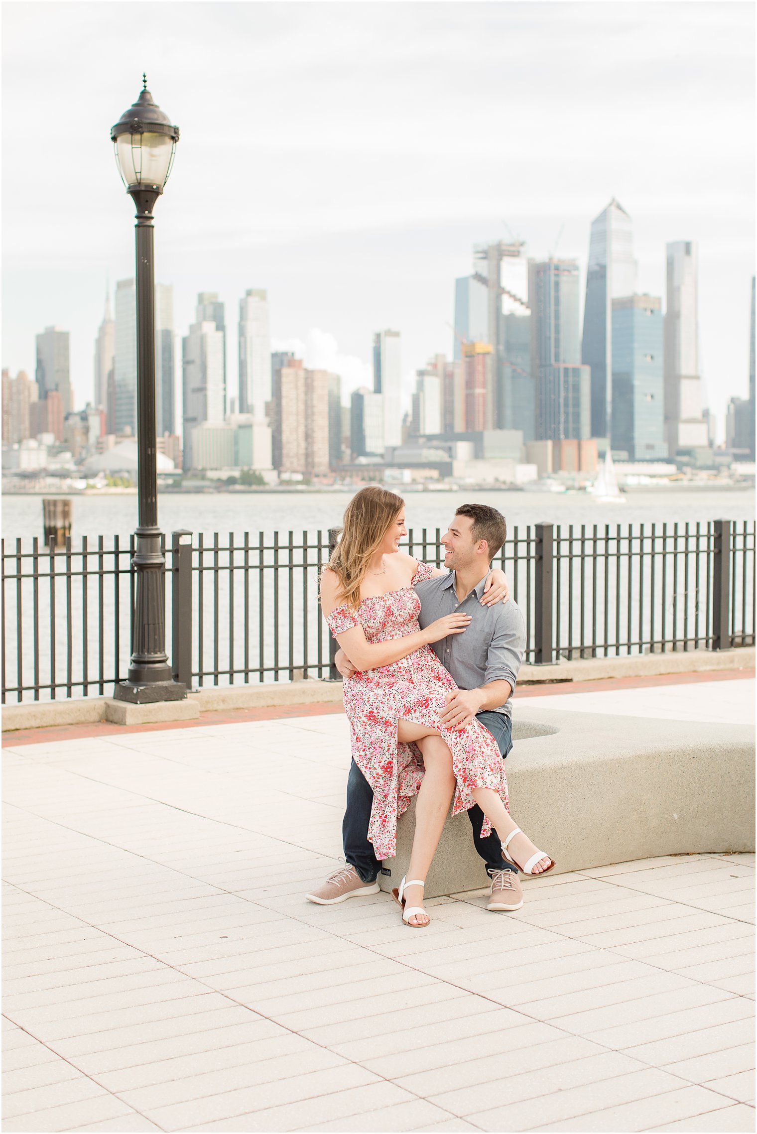 bride sits on groom's lap during Weehawken waterfront engagement session 