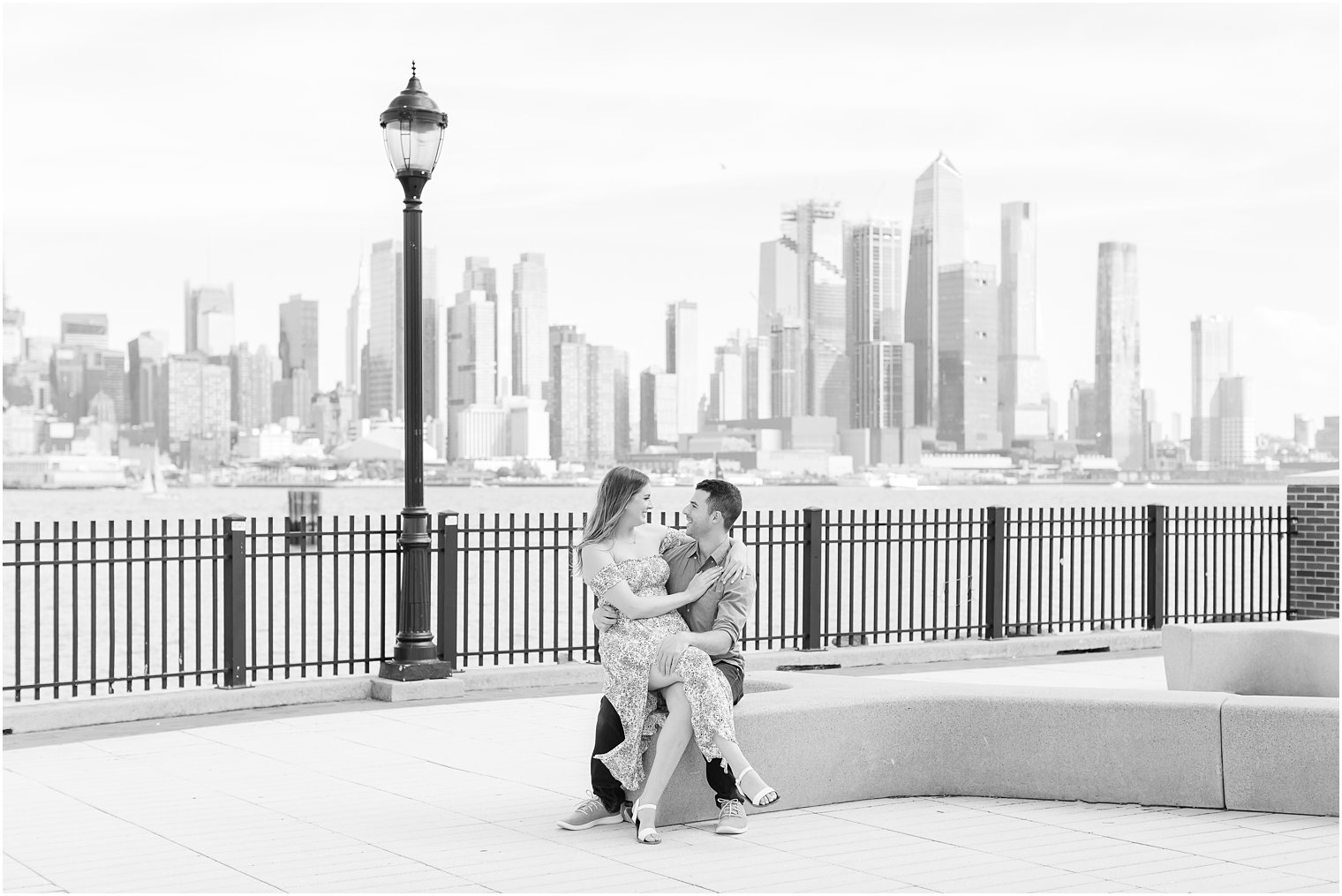 bride sits on groom's lap during Weehawken waterfront engagement session 