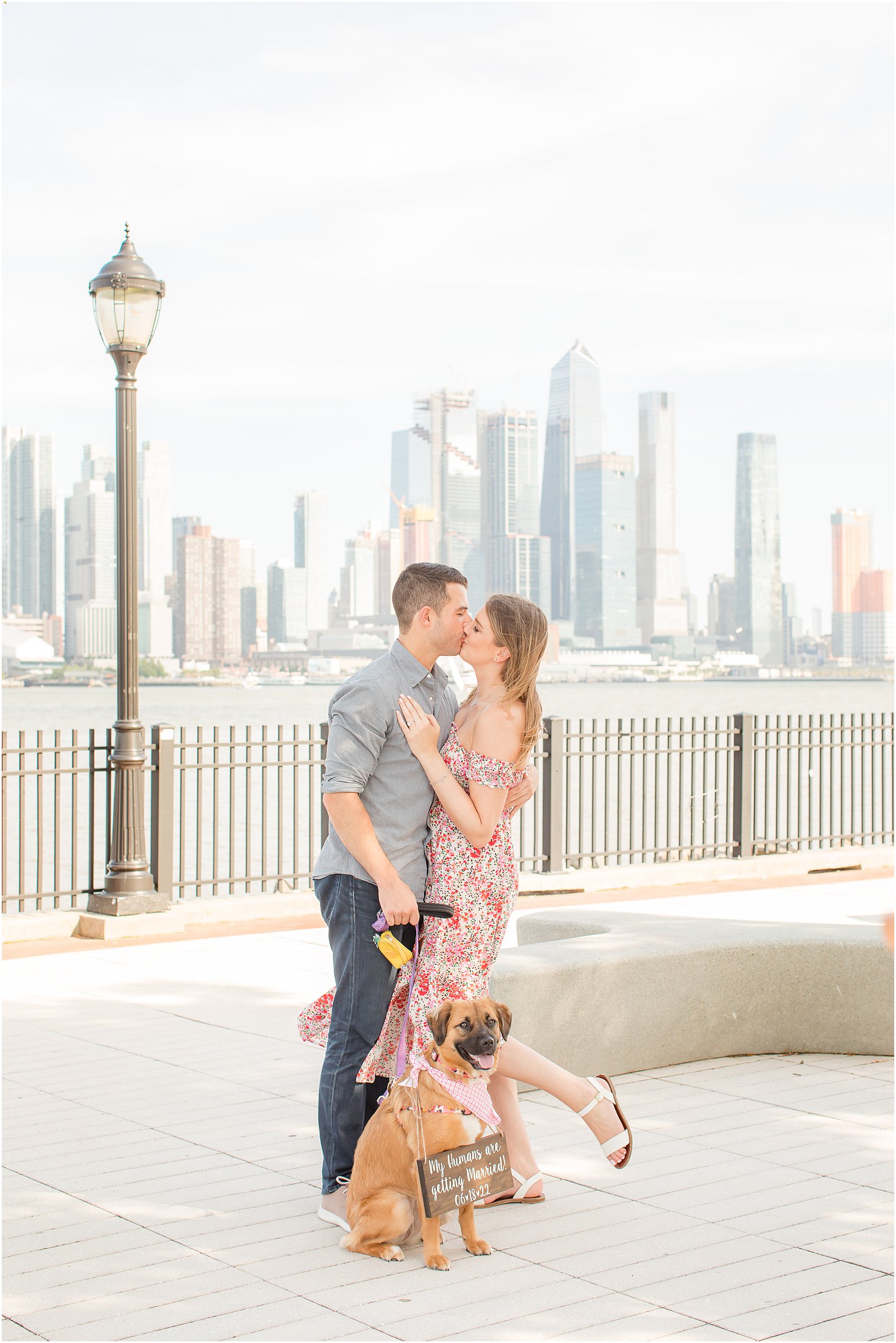 engaged couple kisses while their dog sits at their feet during Weehawken waterfront engagement session