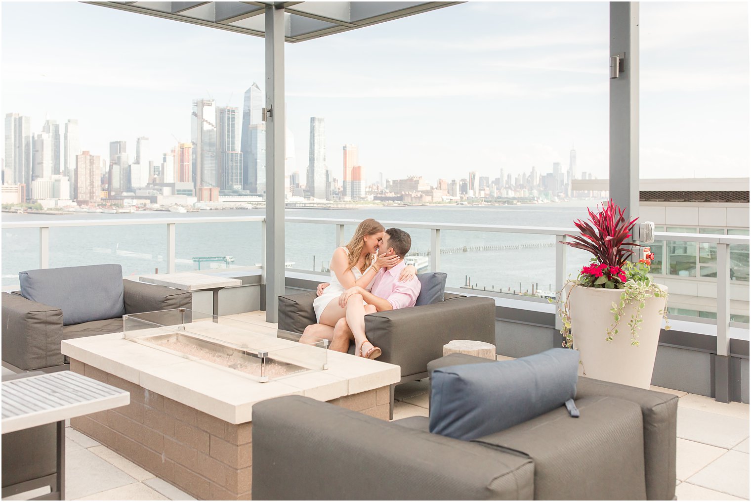 bride sits on groom's lap during Weehawken waterfront engagement session on rooftop bar 