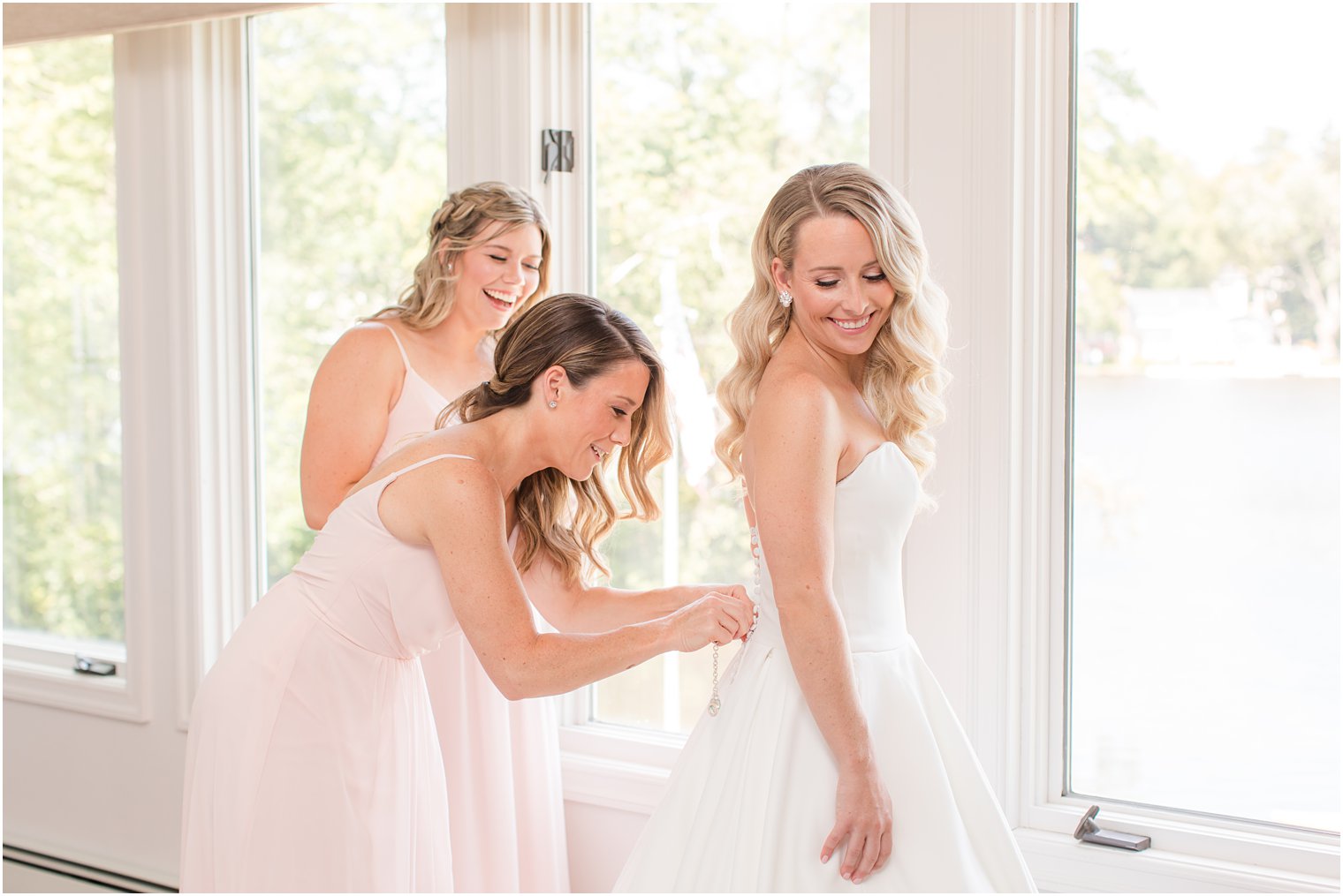 bridesmaids help bride into classic wedding gown