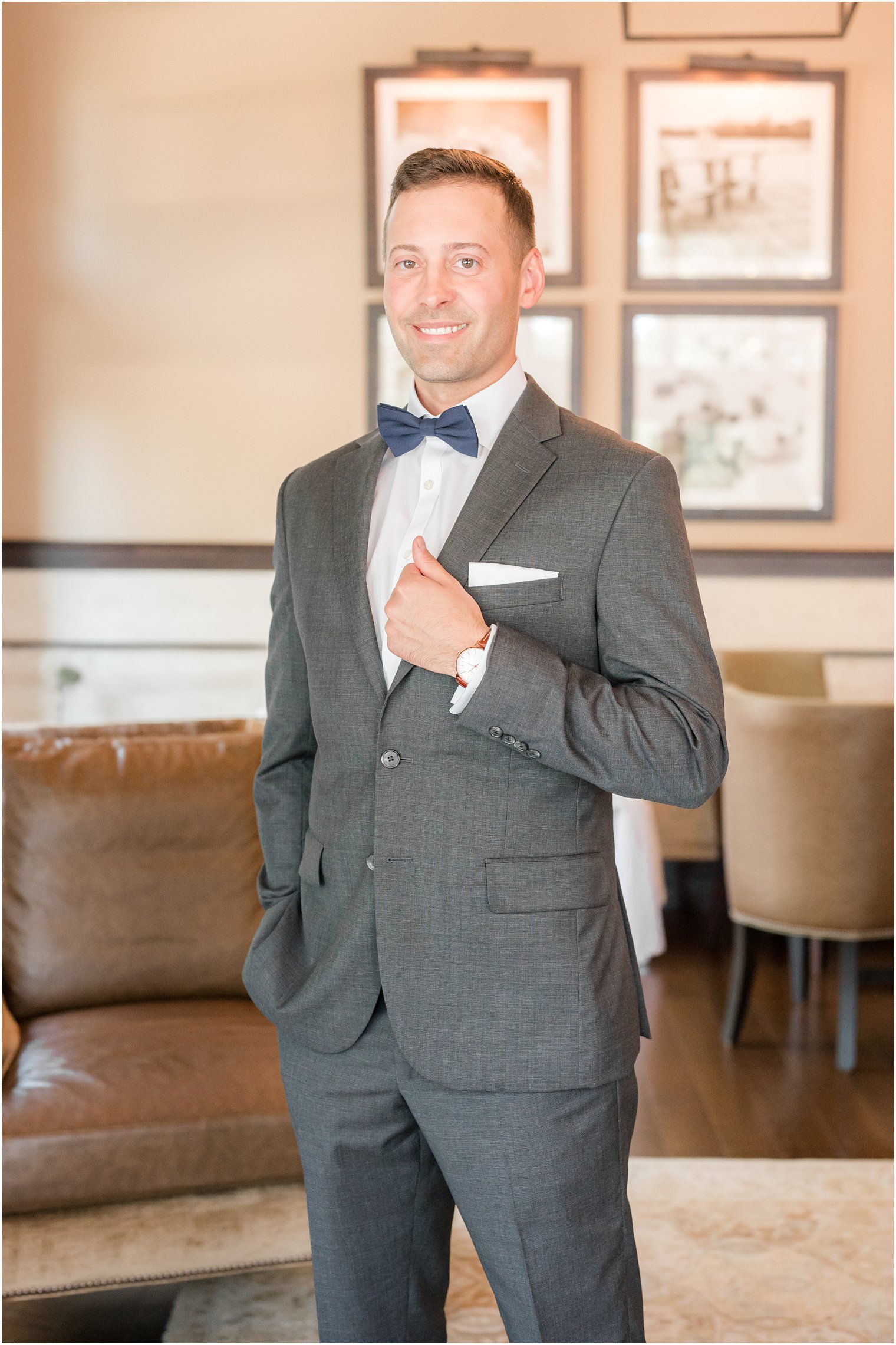groom holds lapel of grey suit with blue bow tie