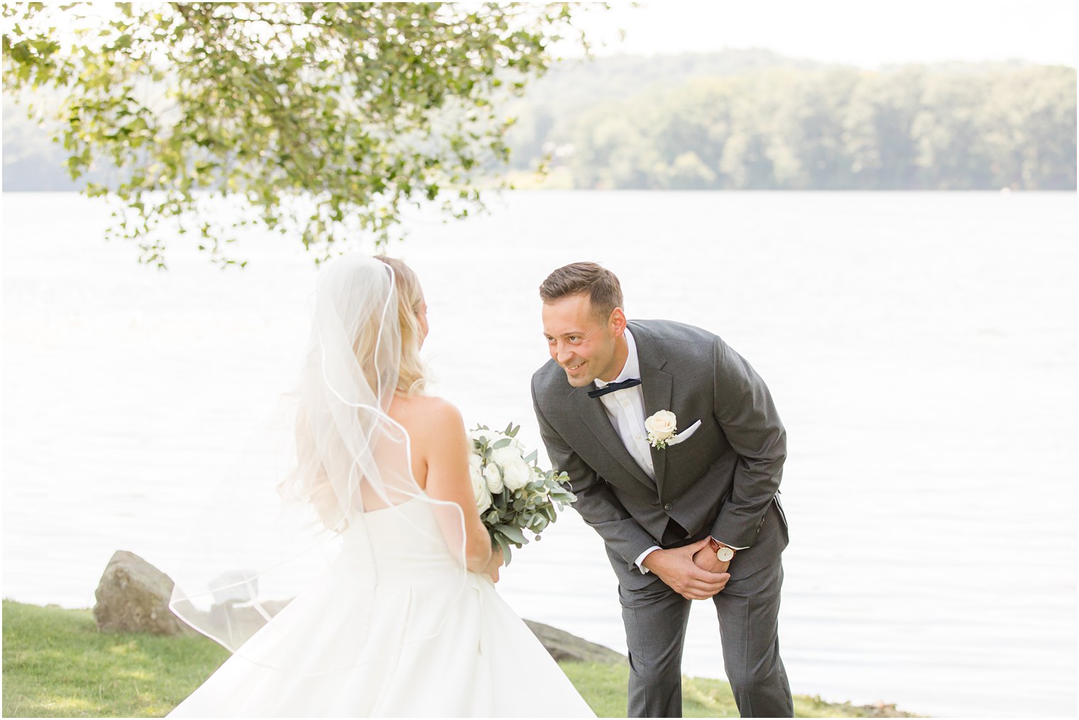 groom smiles at bride during first look along water