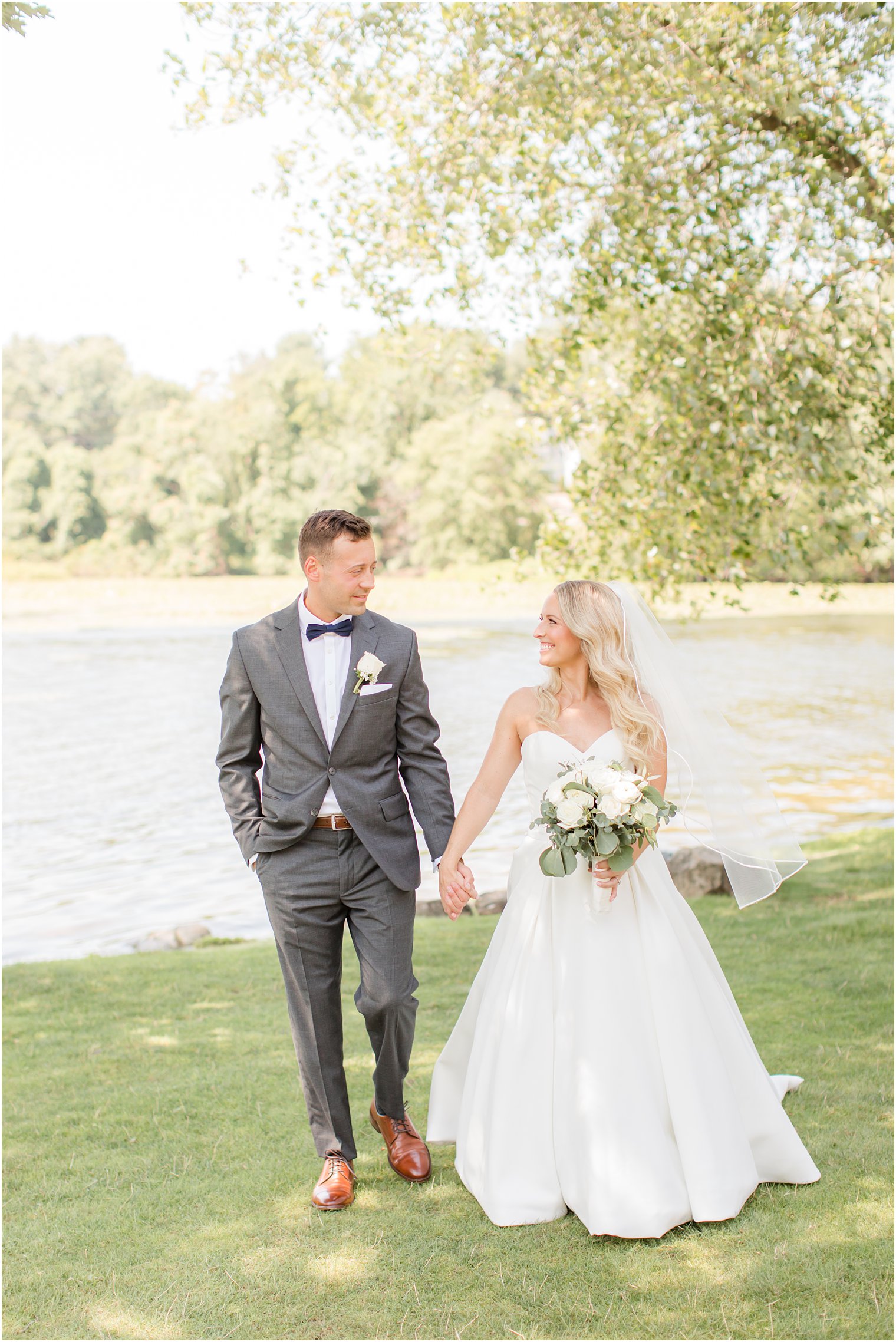 bride and groom hold hands walking along water at Indian Trail Club