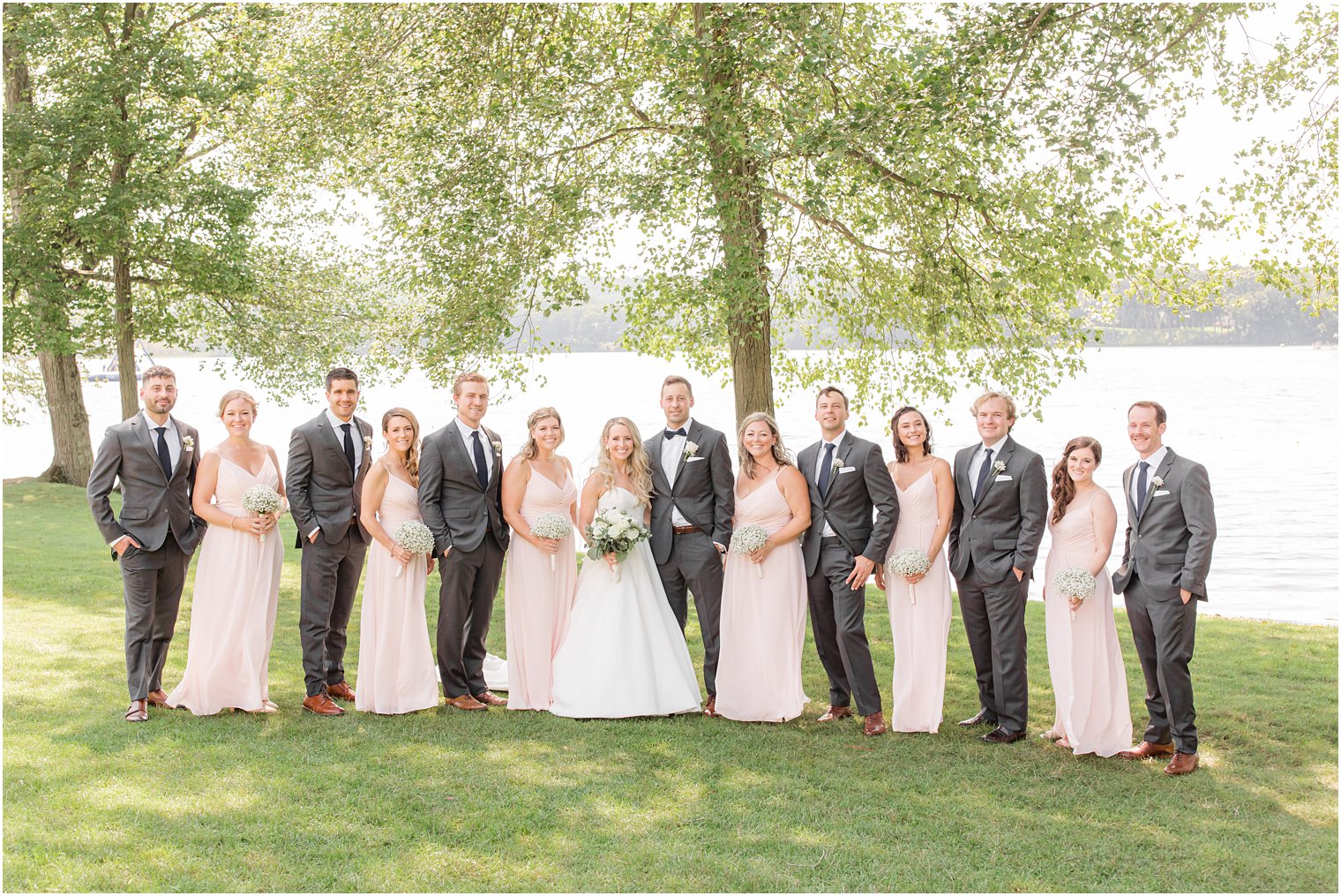 bride and groom stand with wedding party in pastel pink and grey