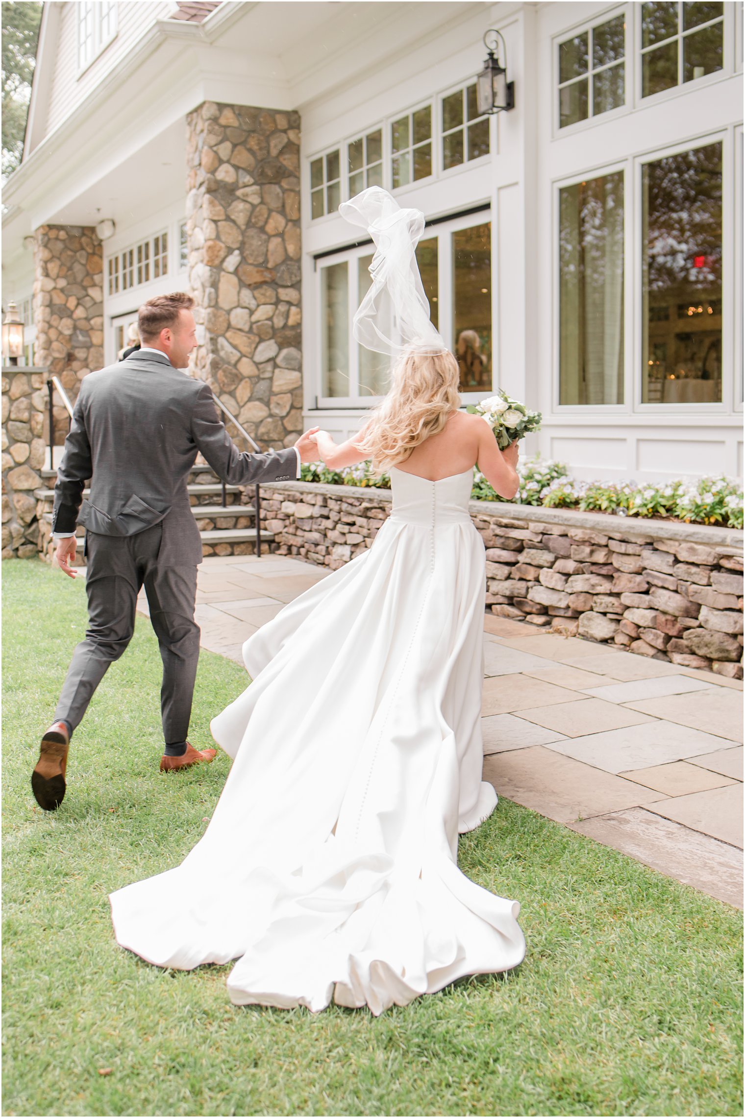 bride and groom walk into Indian Trail Club with bride's veil floating in air