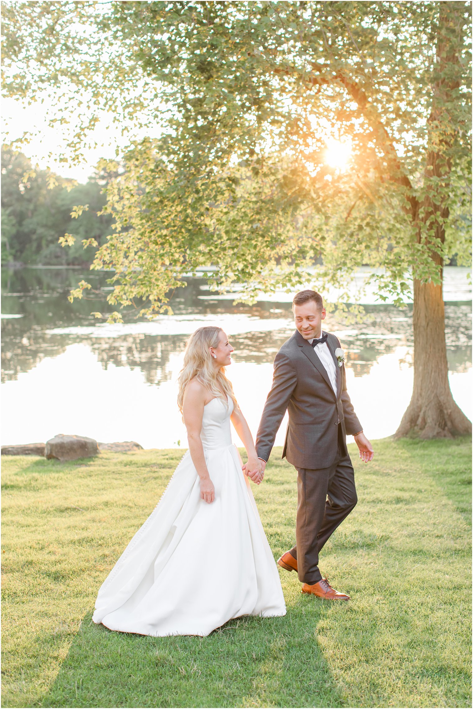 bride and groom walk together at sunset along water at Indian Trail Club