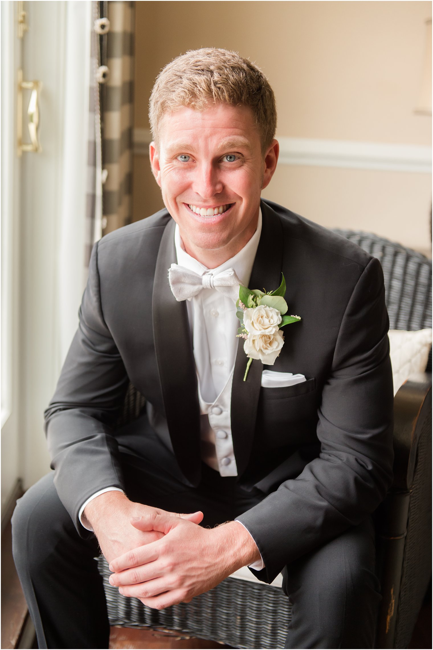groom in classic black suit with white tie sits in library