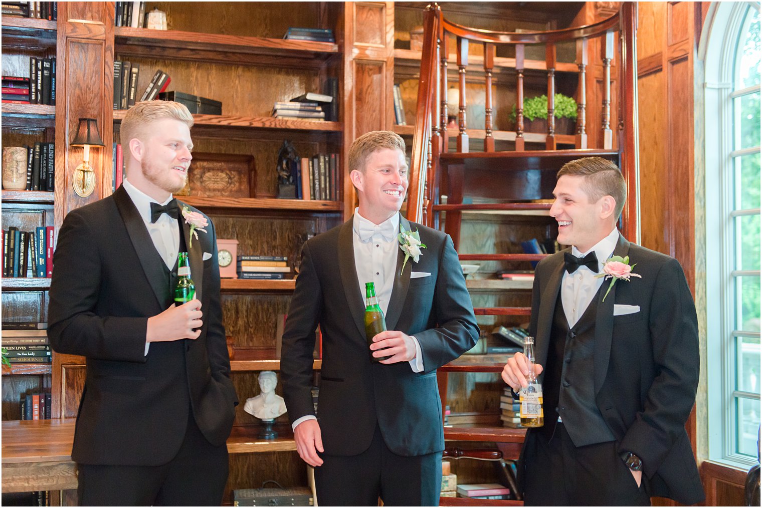 groom laughs with groomsmen drinking beer in library of Ashford Estate