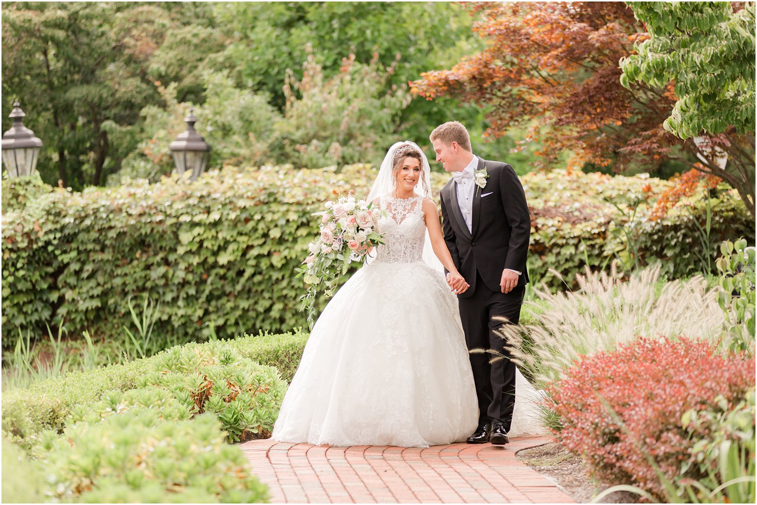 bride and groom hold hands walking through New Jersey garden