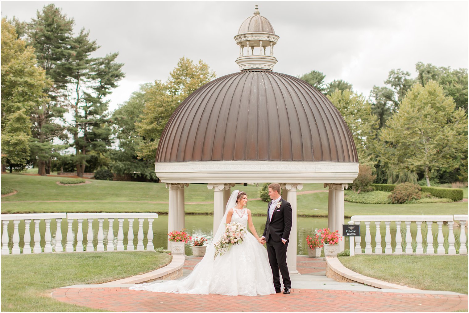 bride and groom hold hands walking outside gazebo 