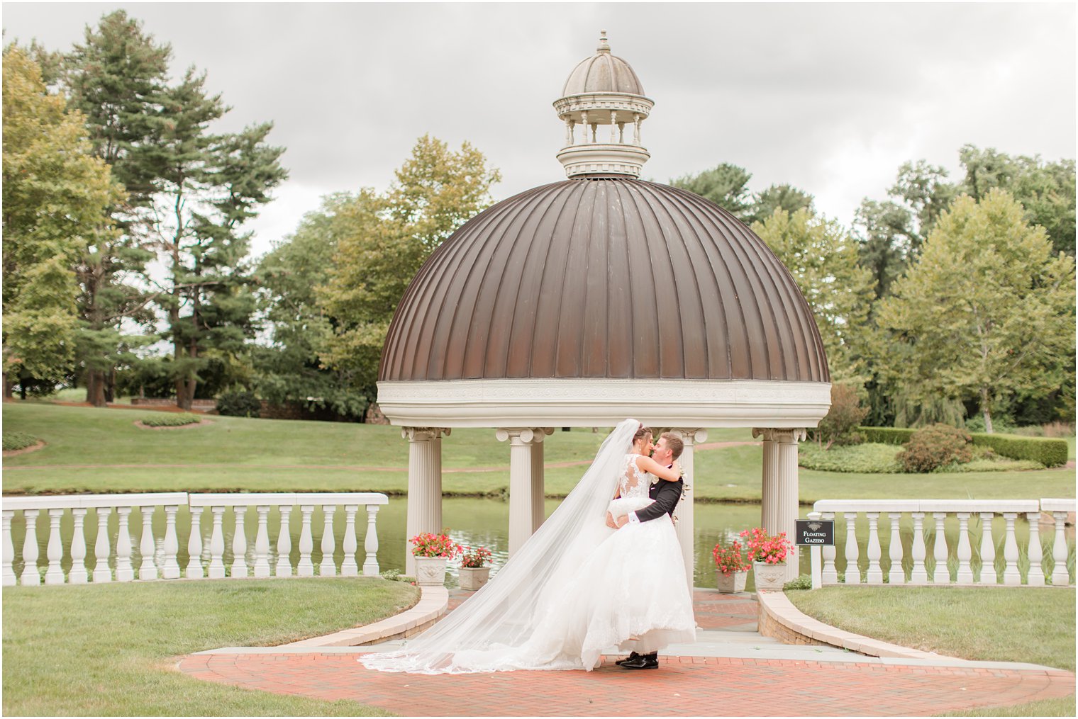 groom lifts bride during NJ wedding portraits by gazebo at Ashford Estate