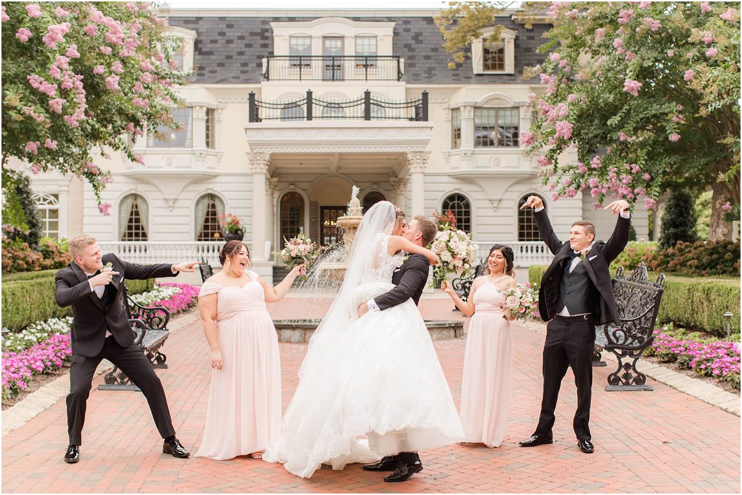 groom lifts bride kissing her while wedding party points at them