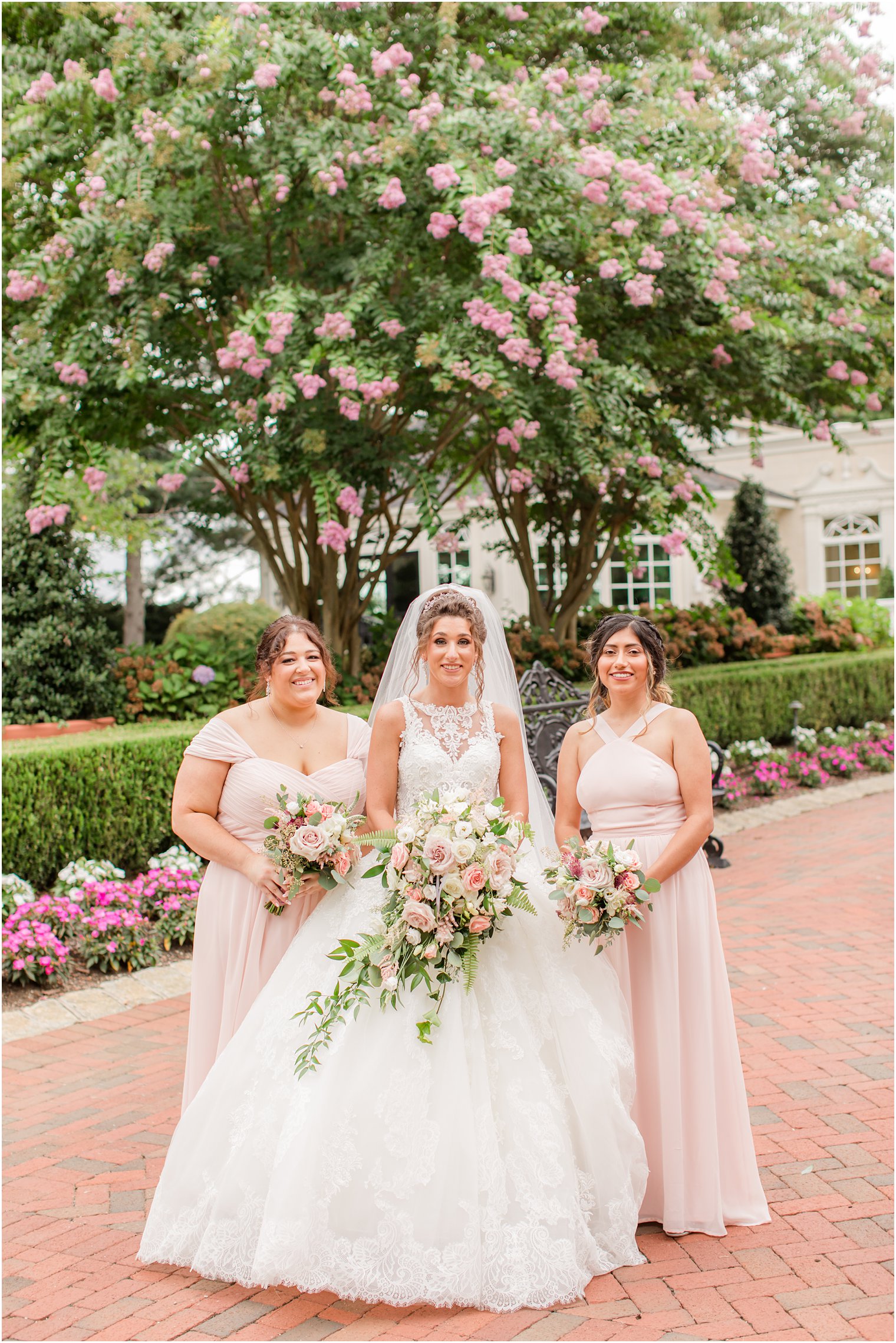 bridesmaids in pastel pink gowns hold bouquets of pink roses