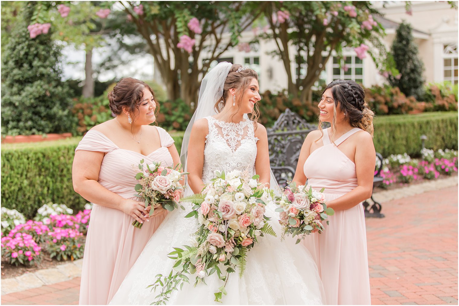 bride smiles at bridesmaids holding pastel pink flowers in pale pink gowns