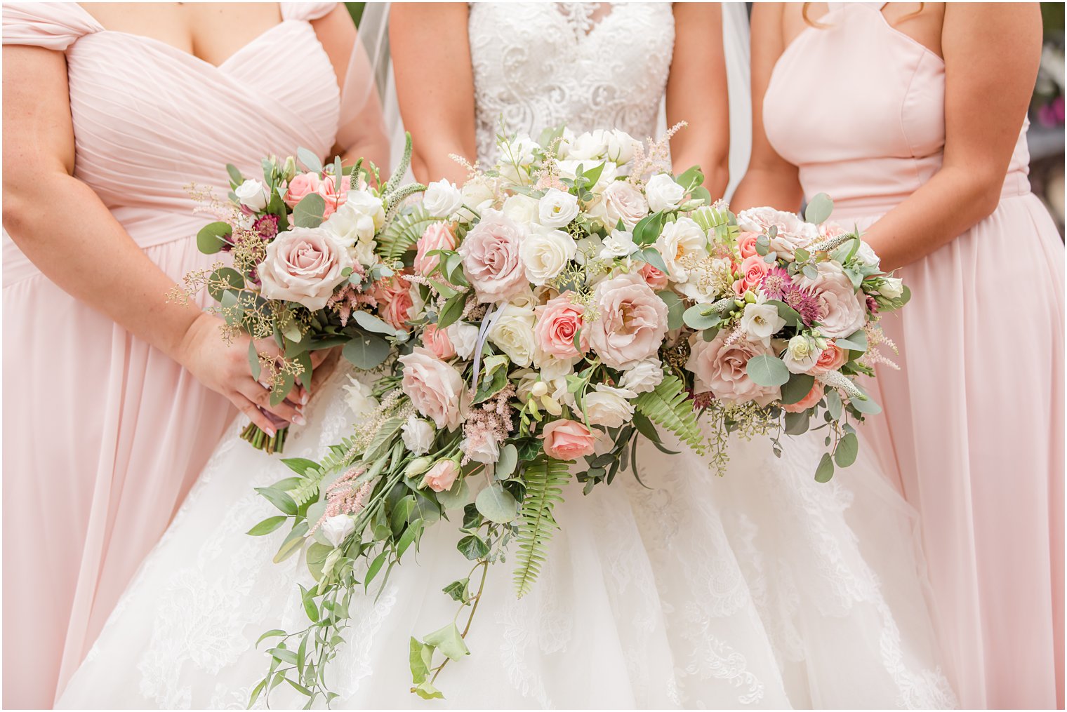 bride and bridesmaids hold bouquets of pastel pink flowers