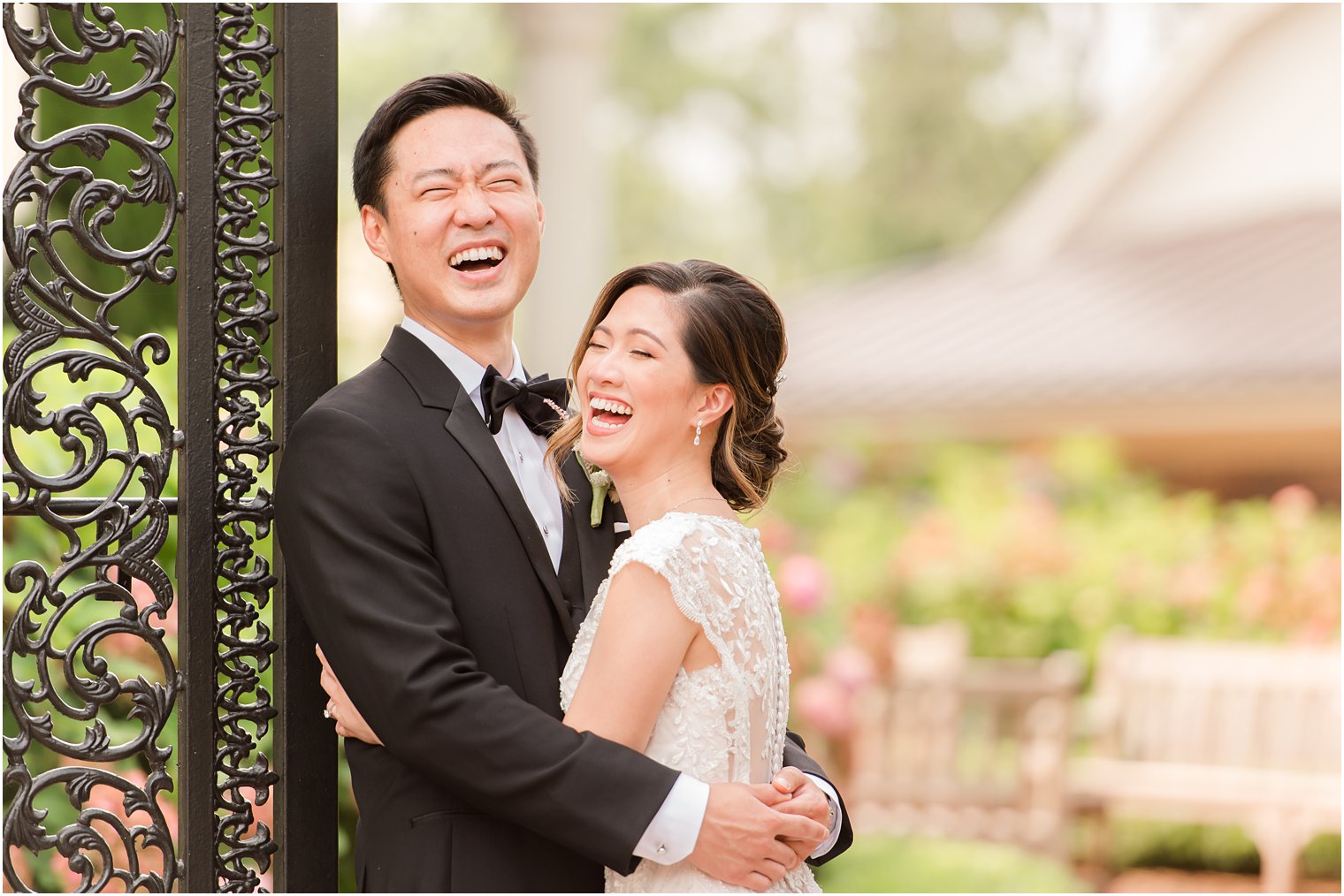 newlyweds laugh while hugging against wrought iron gate in Allentown NJ