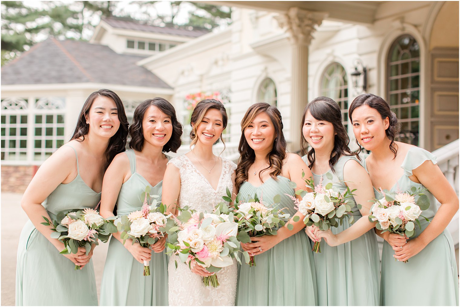 bride poses with bridesmaids in sage green dresses outside Ashford Estate