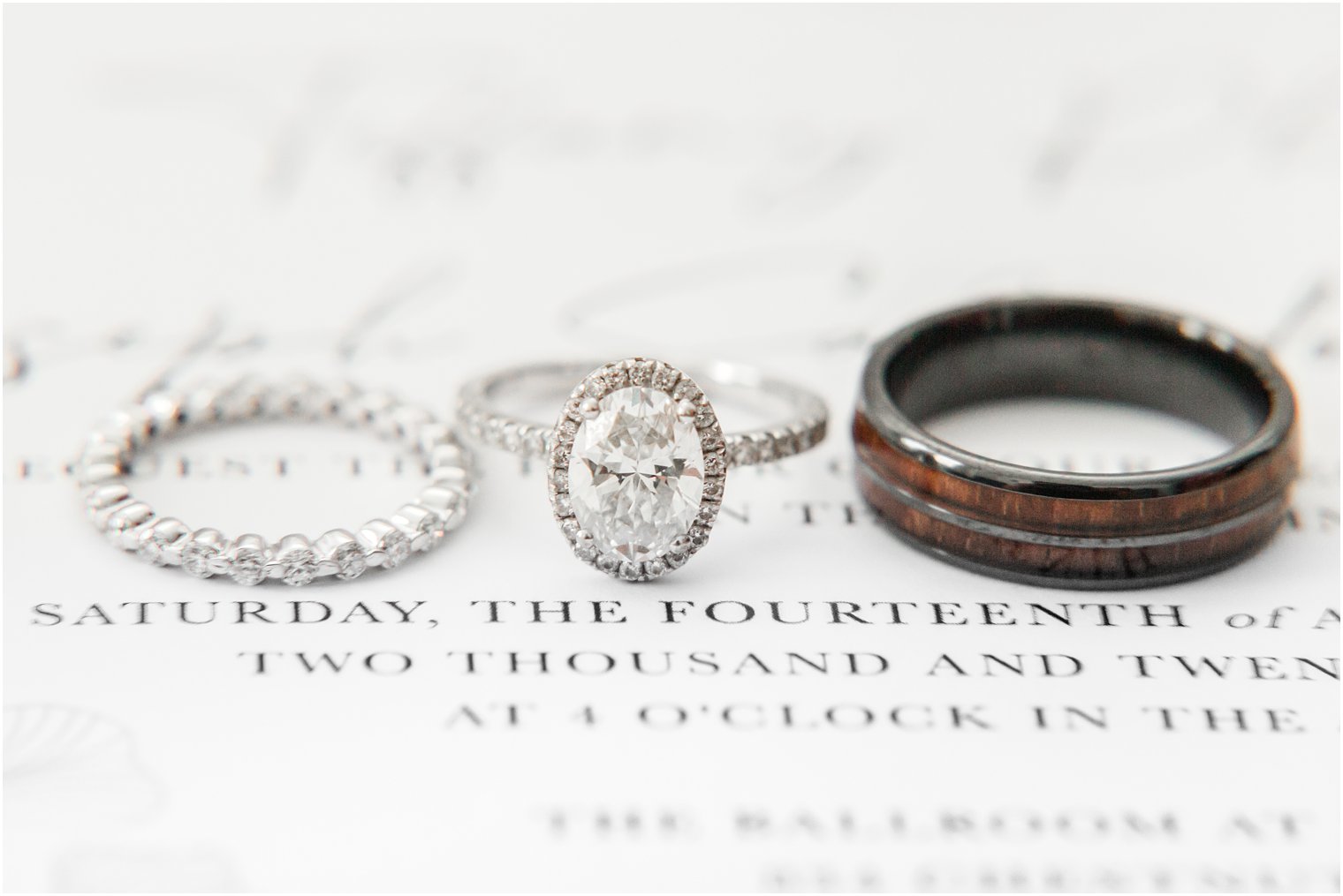 bride and groom's wedding rings rest on wedding invite 