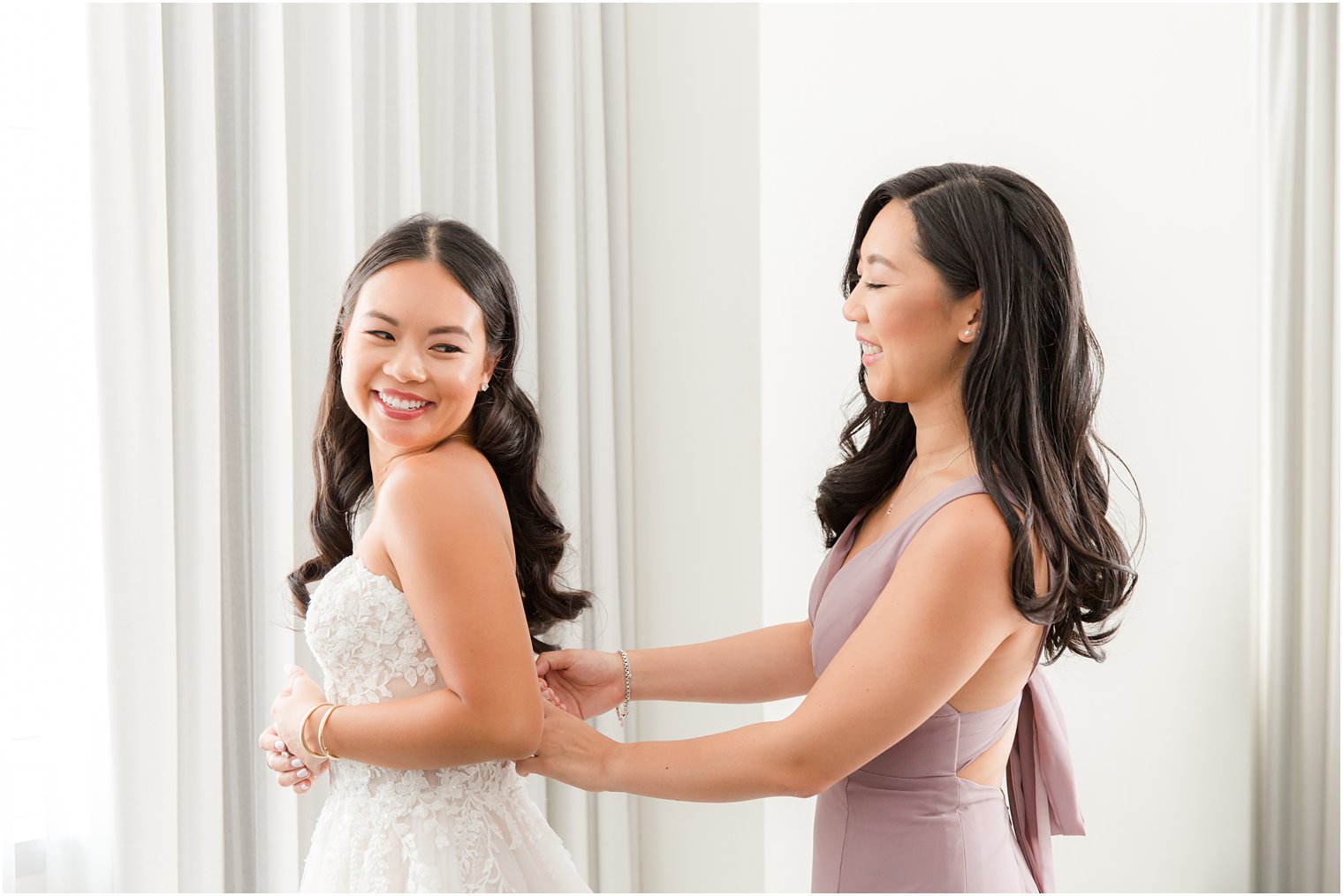 bridesmaid in mauve gown helps bride with wedding dress