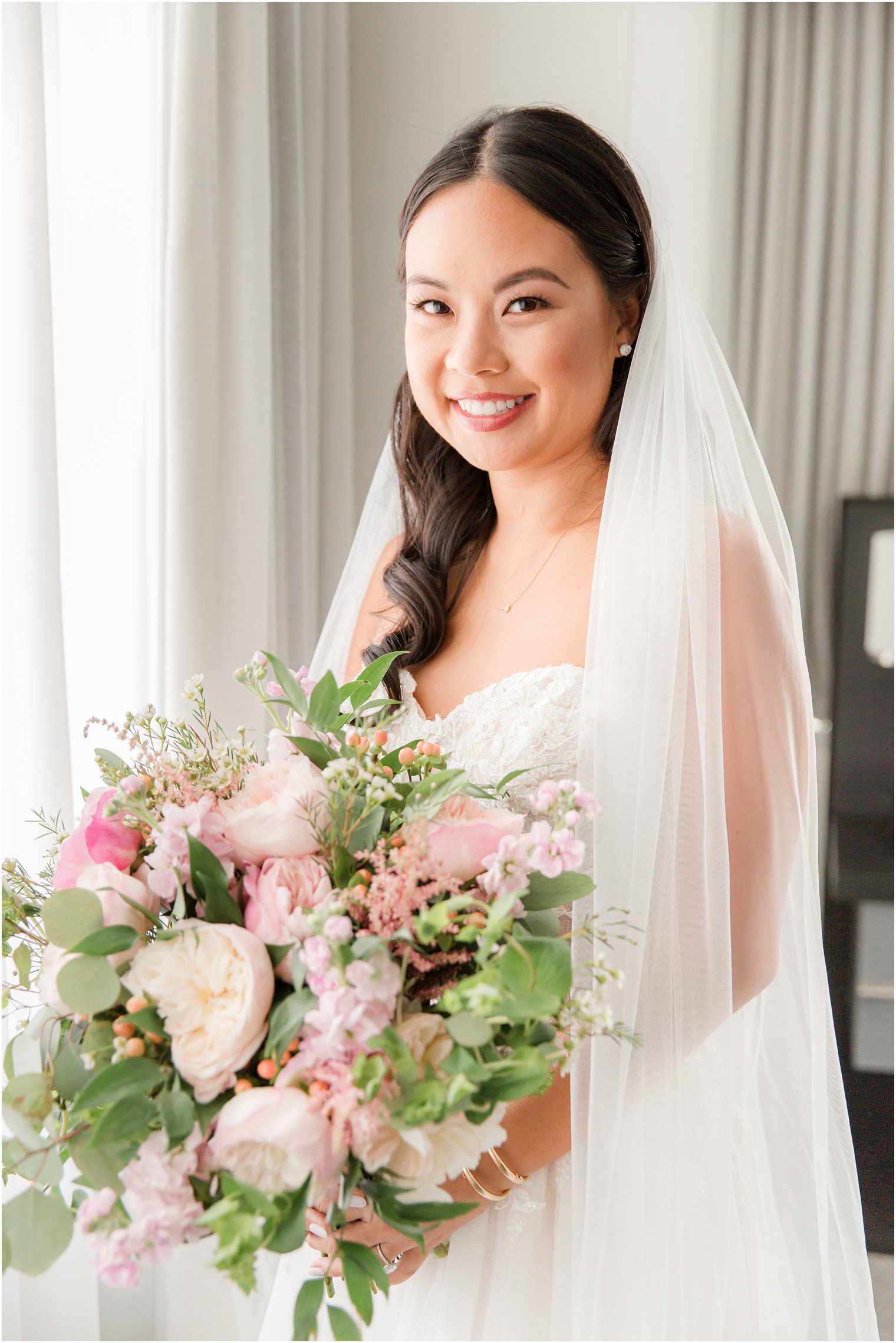 bride holds bouquet of pink flowers with veil around shoulders
