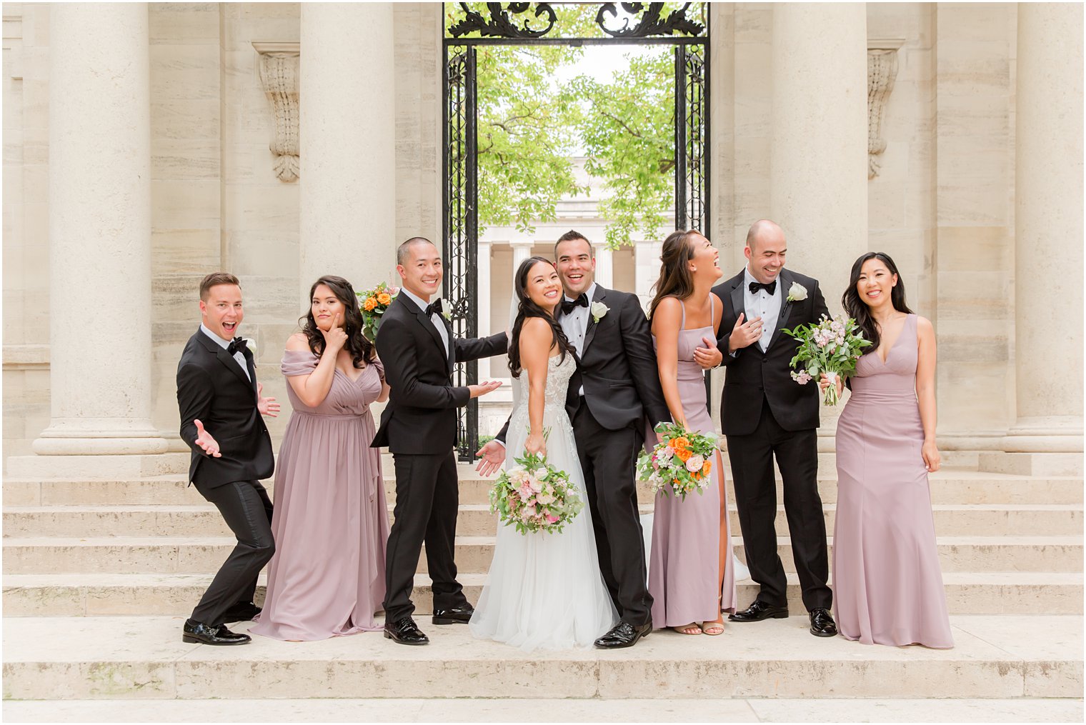newlyweds laugh with wedding party on steps of Rodin Museum