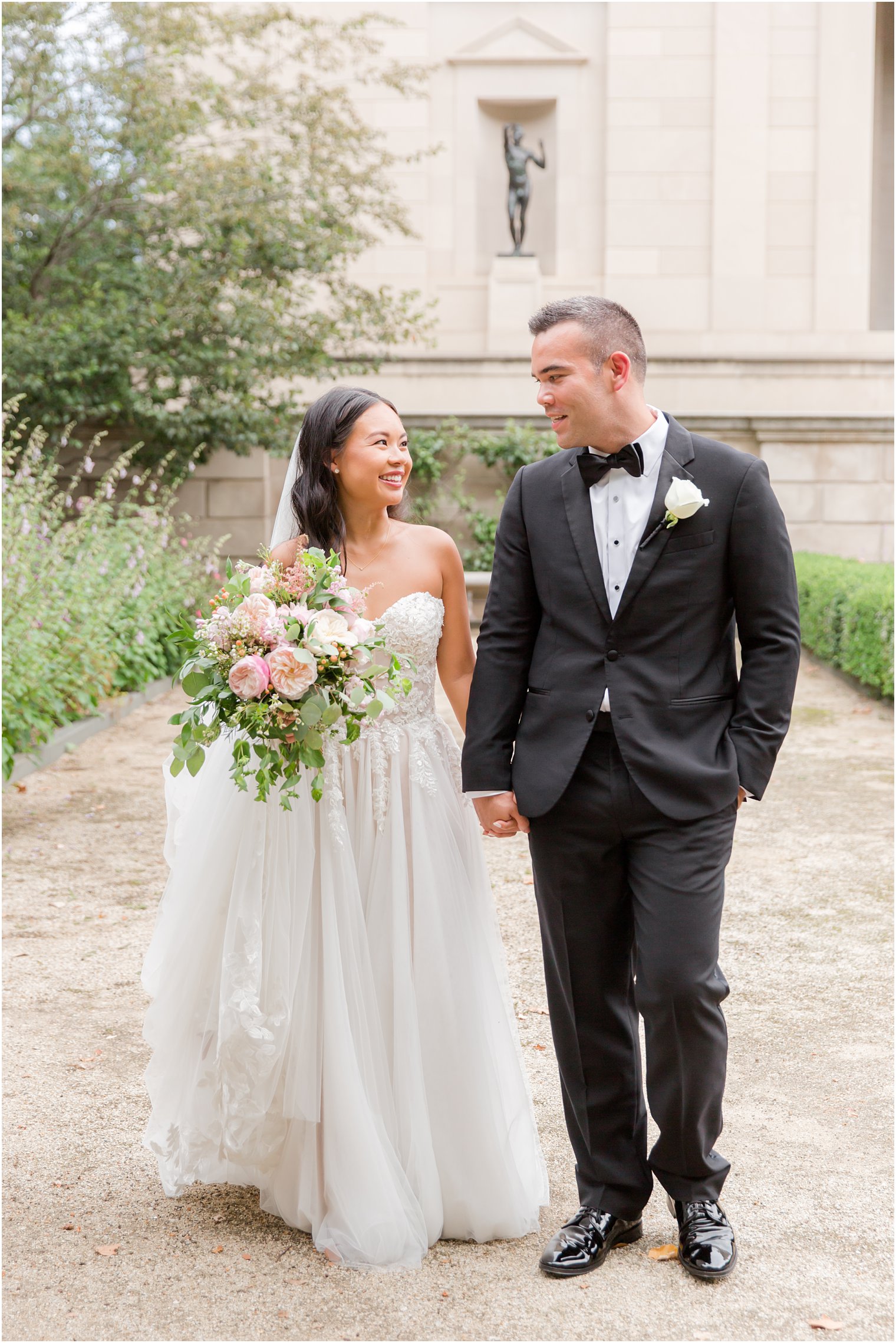 bride and groom hold hands walking through gardens of Rodin Museum