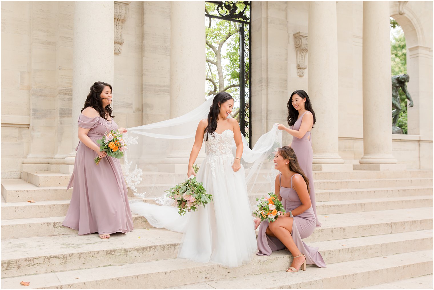 bridesmaids in mauve hold bride's veil on steps of Rodin Museum