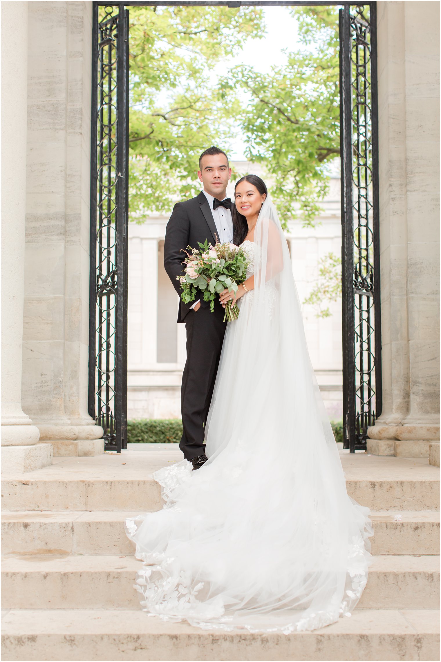 bride and groom pose on steps of Rodin Museum between wrought iron gates