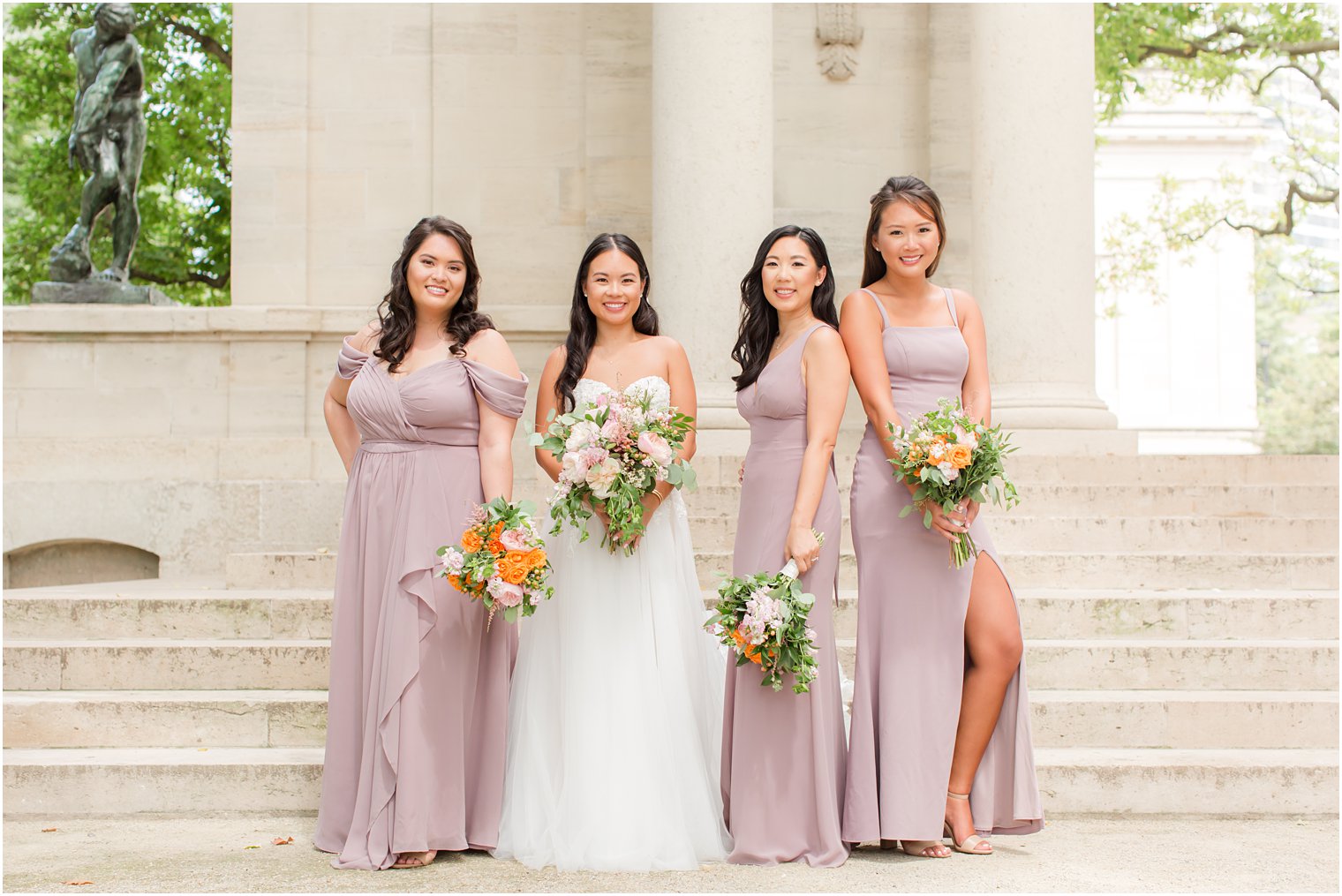 bride poses with three bridesmaids in mauve gowns on steps of Rodin Museum