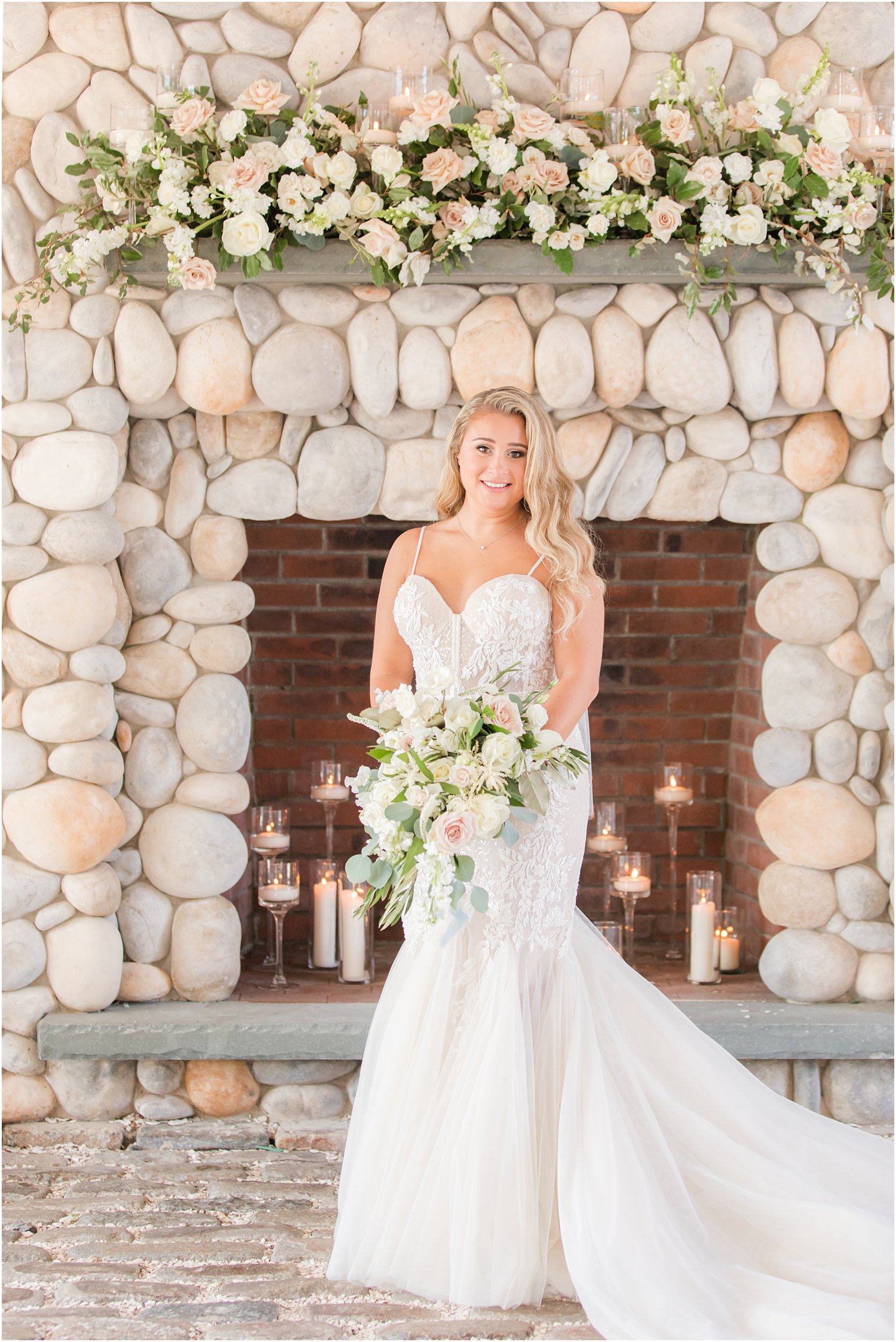 bride poses in front of stone fireplace holding cascading bouquet 