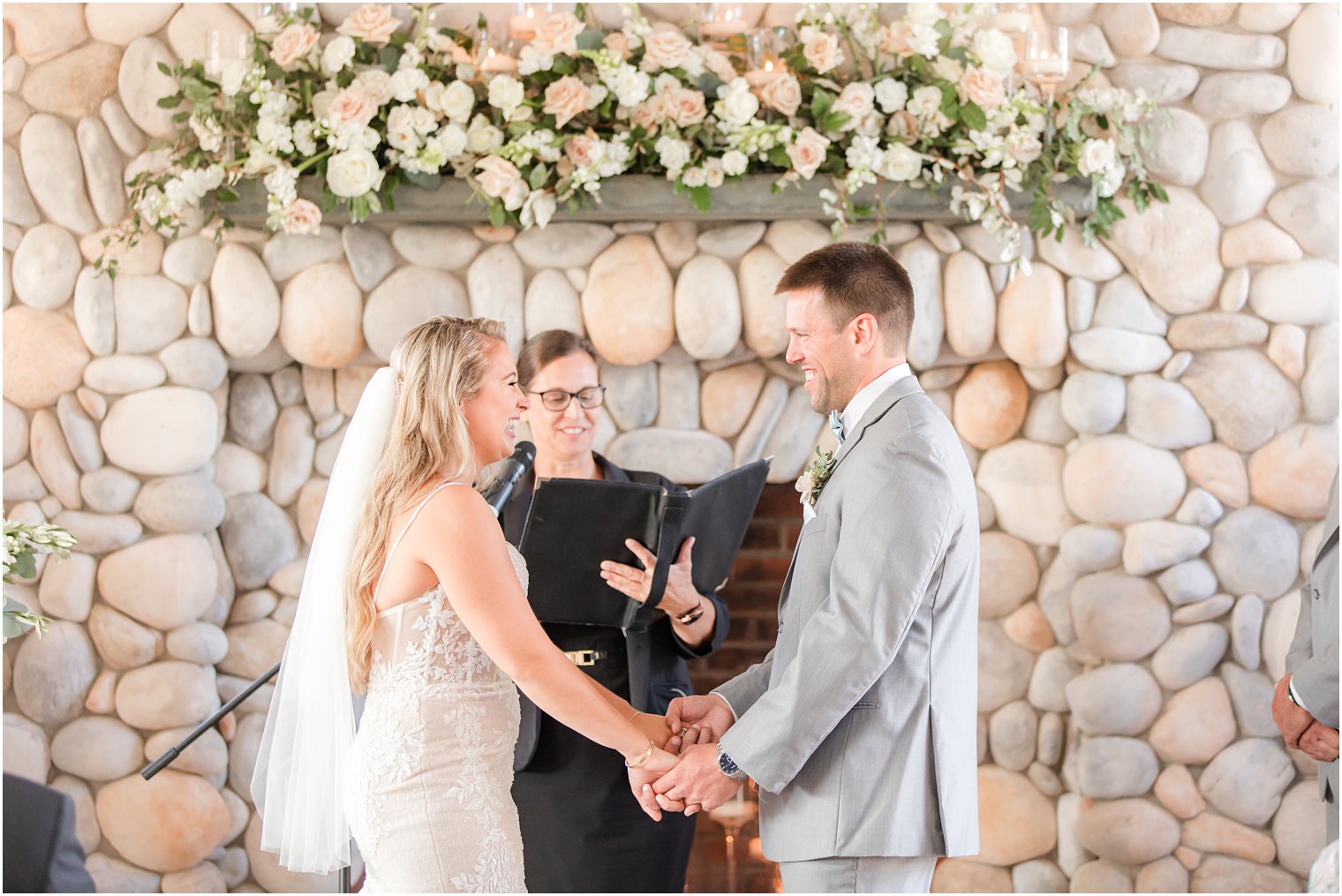 newlyweds hold hands and exchange vows by stone fireplace at wedding ceremony in Manahawkin NJ