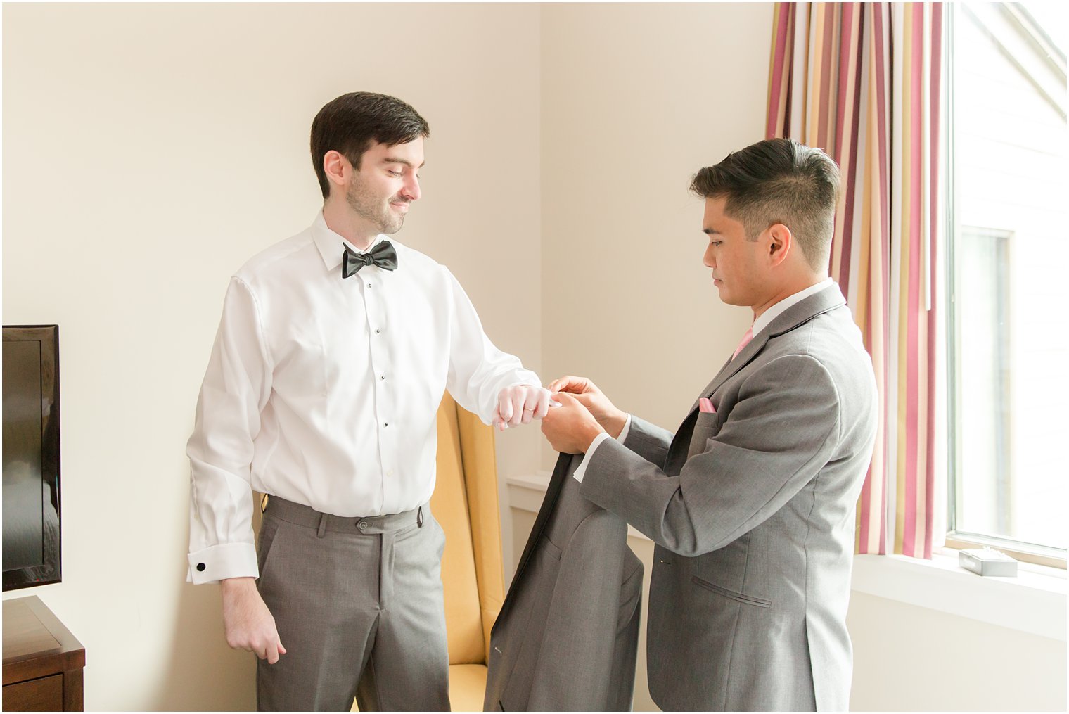 groomsman helps groom into custom suit jacket before NJ wedding