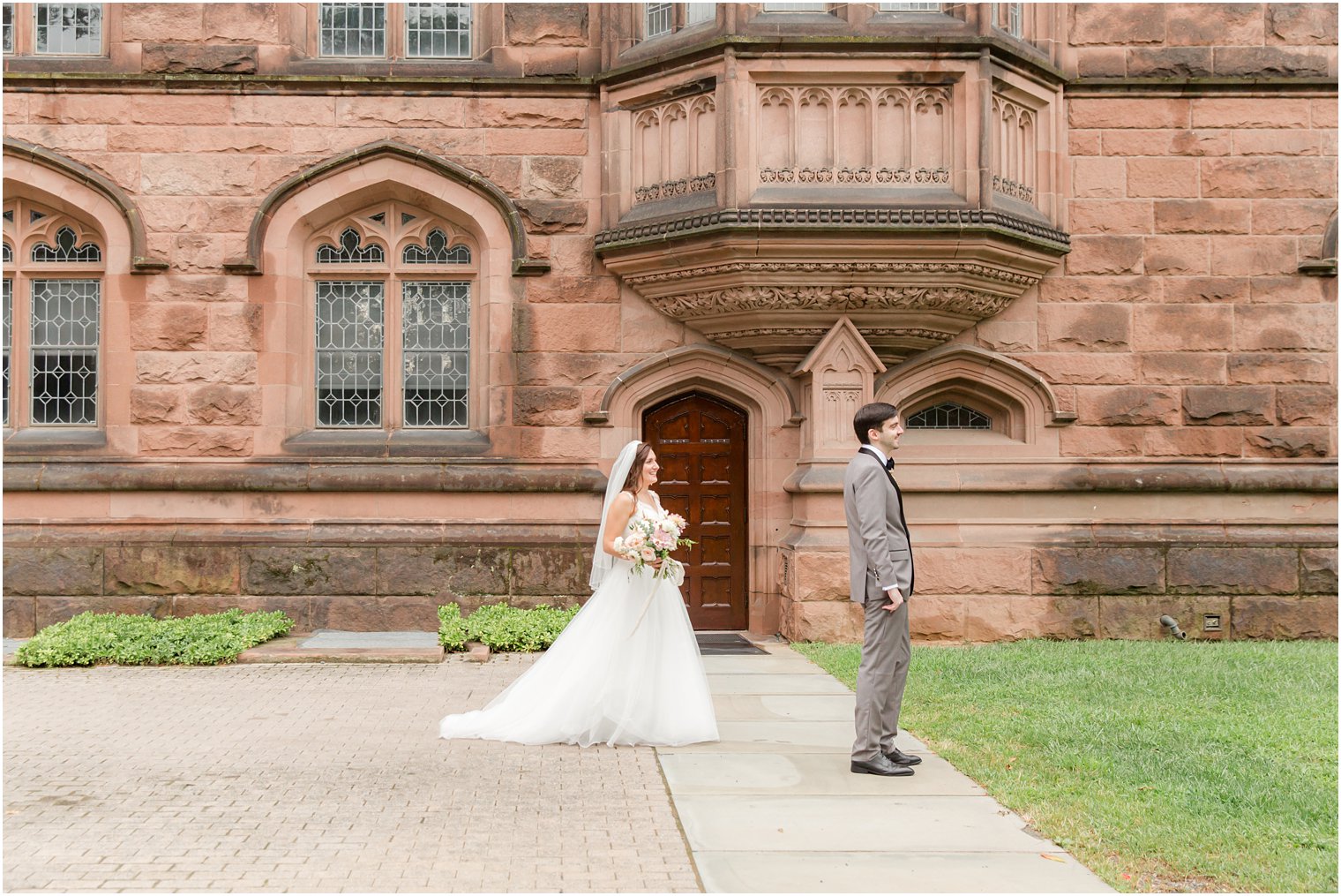 bride approaches groom for first look outside brick building at Princeton University