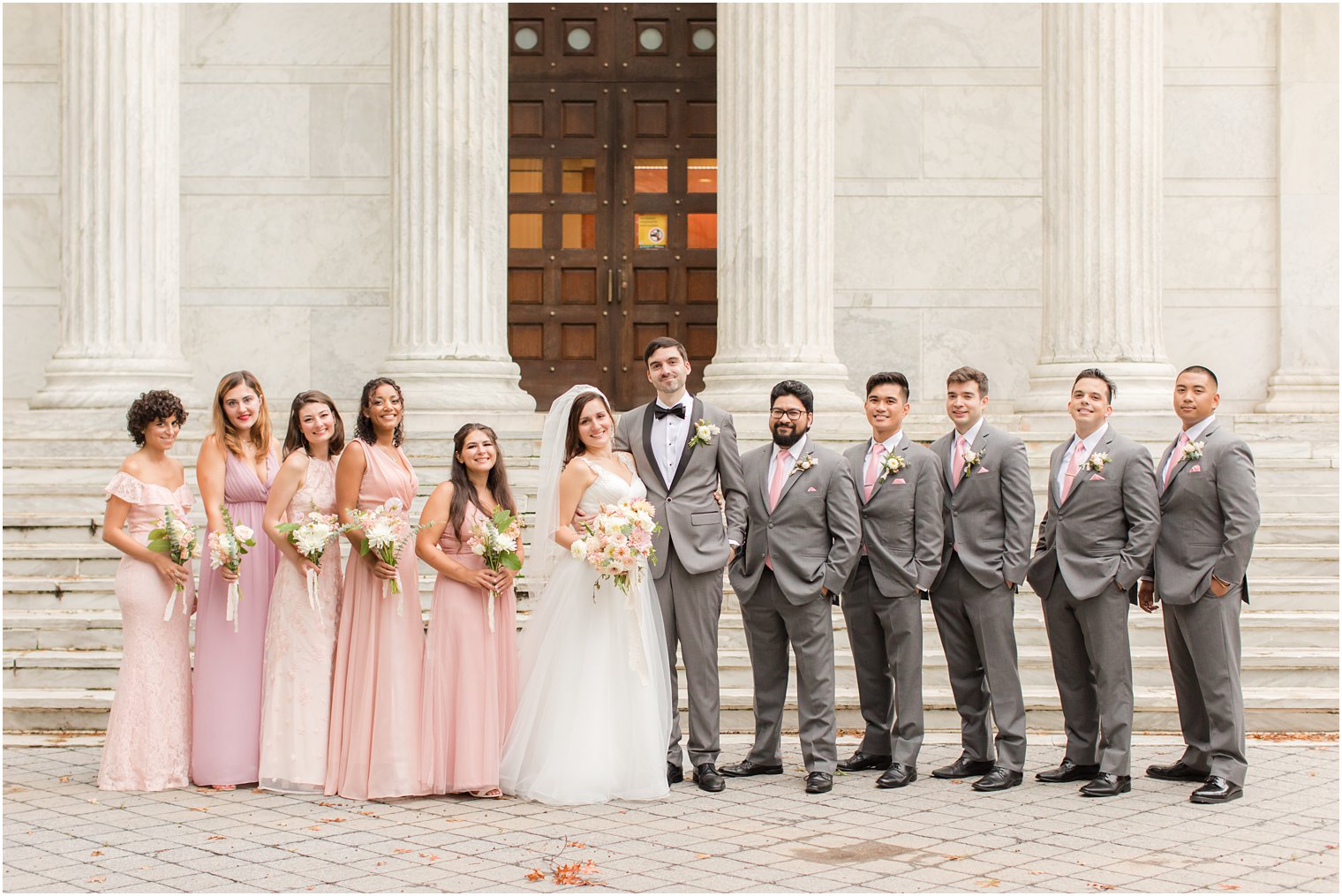 newlyweds pose on steps of Princeton University with wedding party in pink and grey