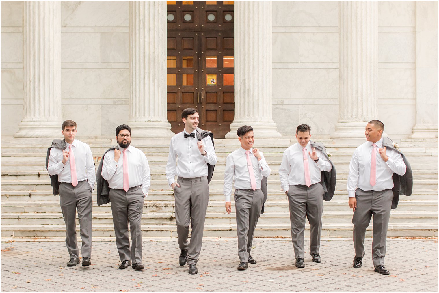 groom walks with groomsmen with suit jackets over their shoulders at Princeton University