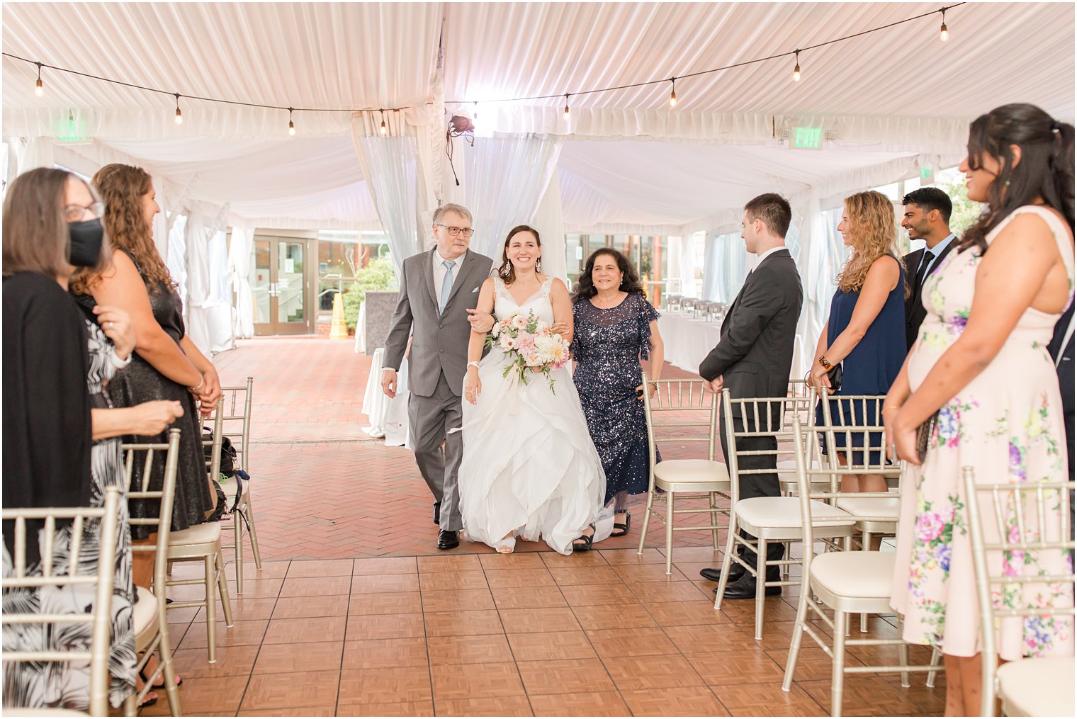 bride walks down aisle with parents during Jewish wedding ceremony