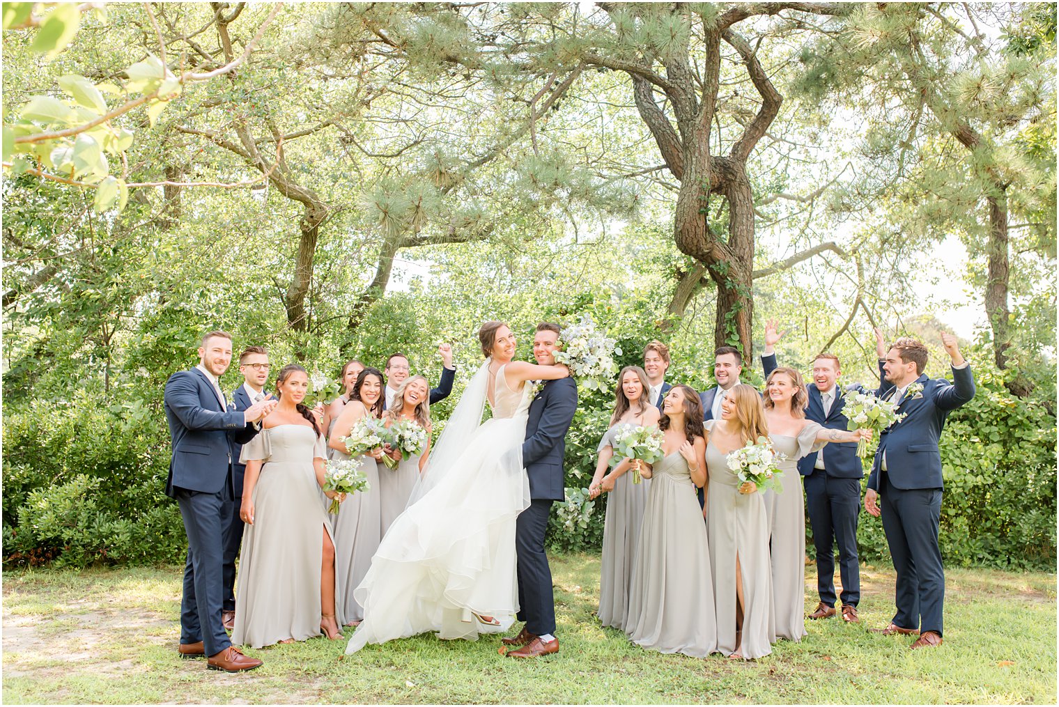 groom lifts up bride during photos with wedding party in NJ park