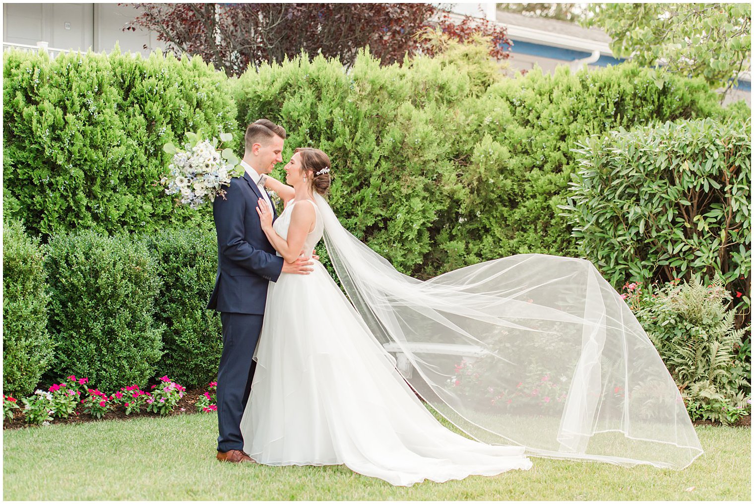 bride and groom stand together with bride's veil floating behind them