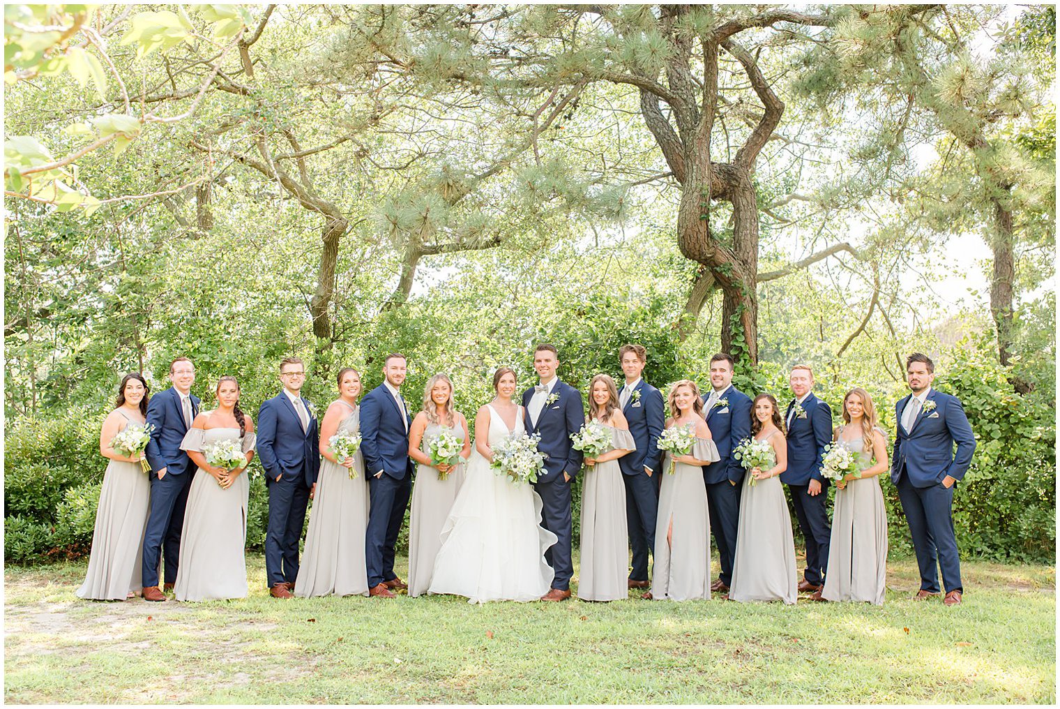 bride and groom pose with wedding party in grey dresses and navy suits