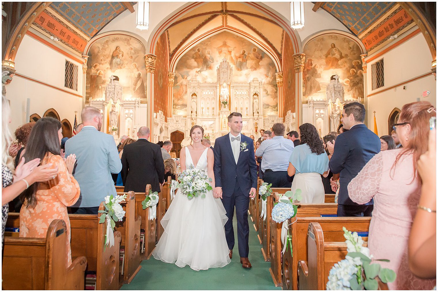 newlyweds hold hands walking up aisle after traditional church wedding in NJ