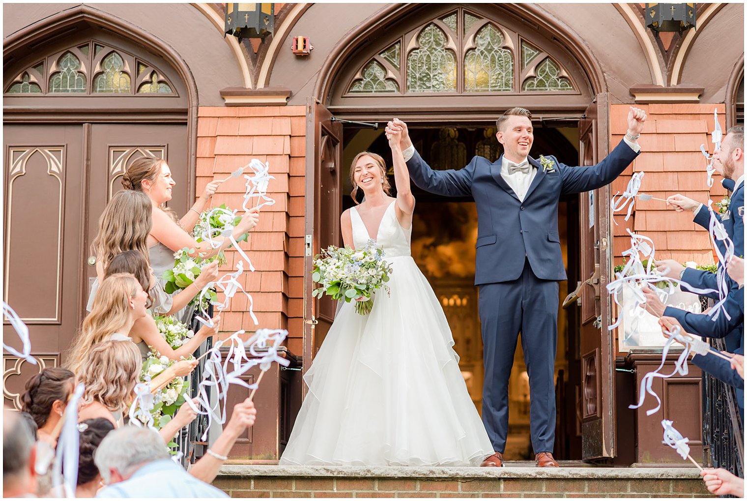 newlyweds laugh leaving church with guests waving ribbons