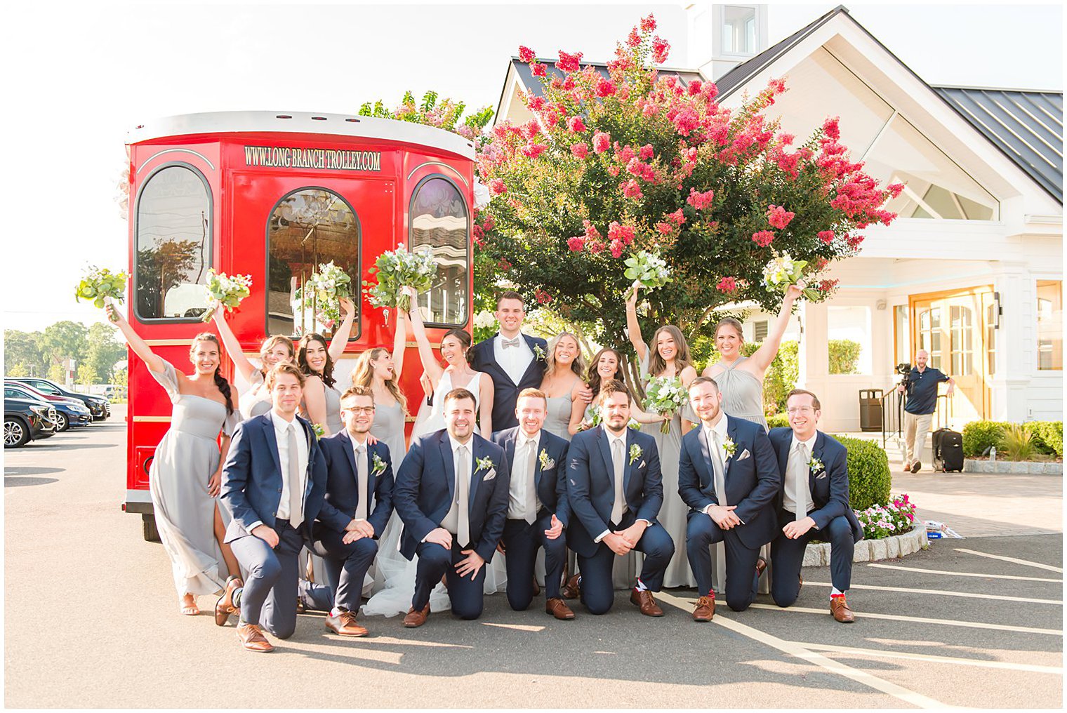 bride and groom pose with wedding party outside red trolley