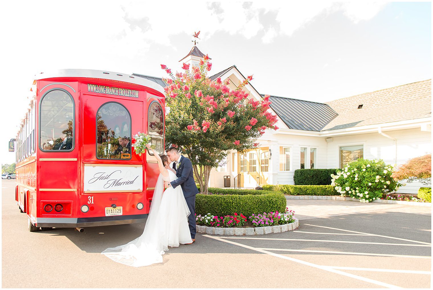 newlyweds kiss by red Long Branch Trolley with bride holding bouquet in air
