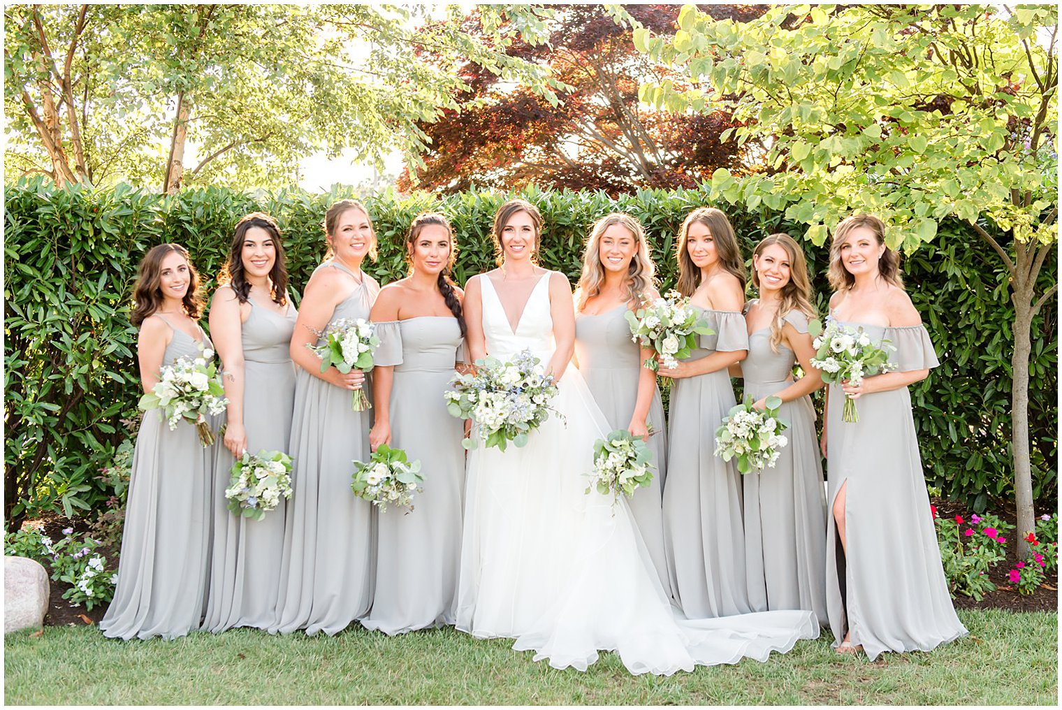 bride poses with bridesmaids in mismatched grey gowns outside Crystal Point Yacht Club