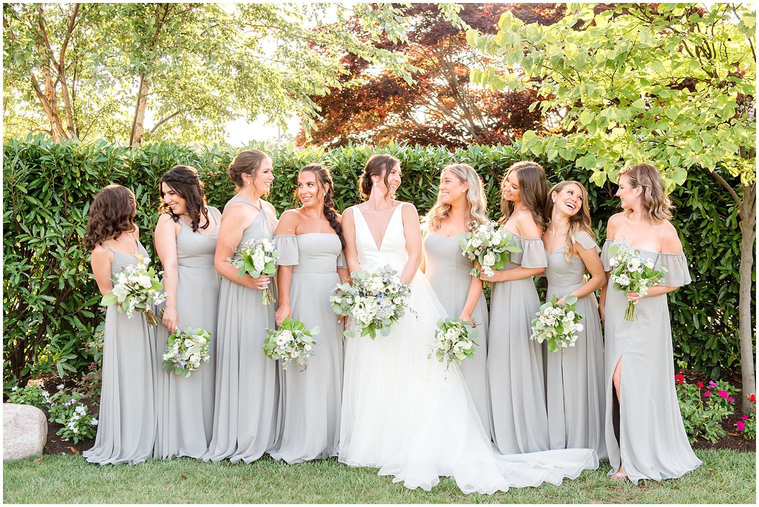 bride and bridesmaids laugh holding bouquets in gardens